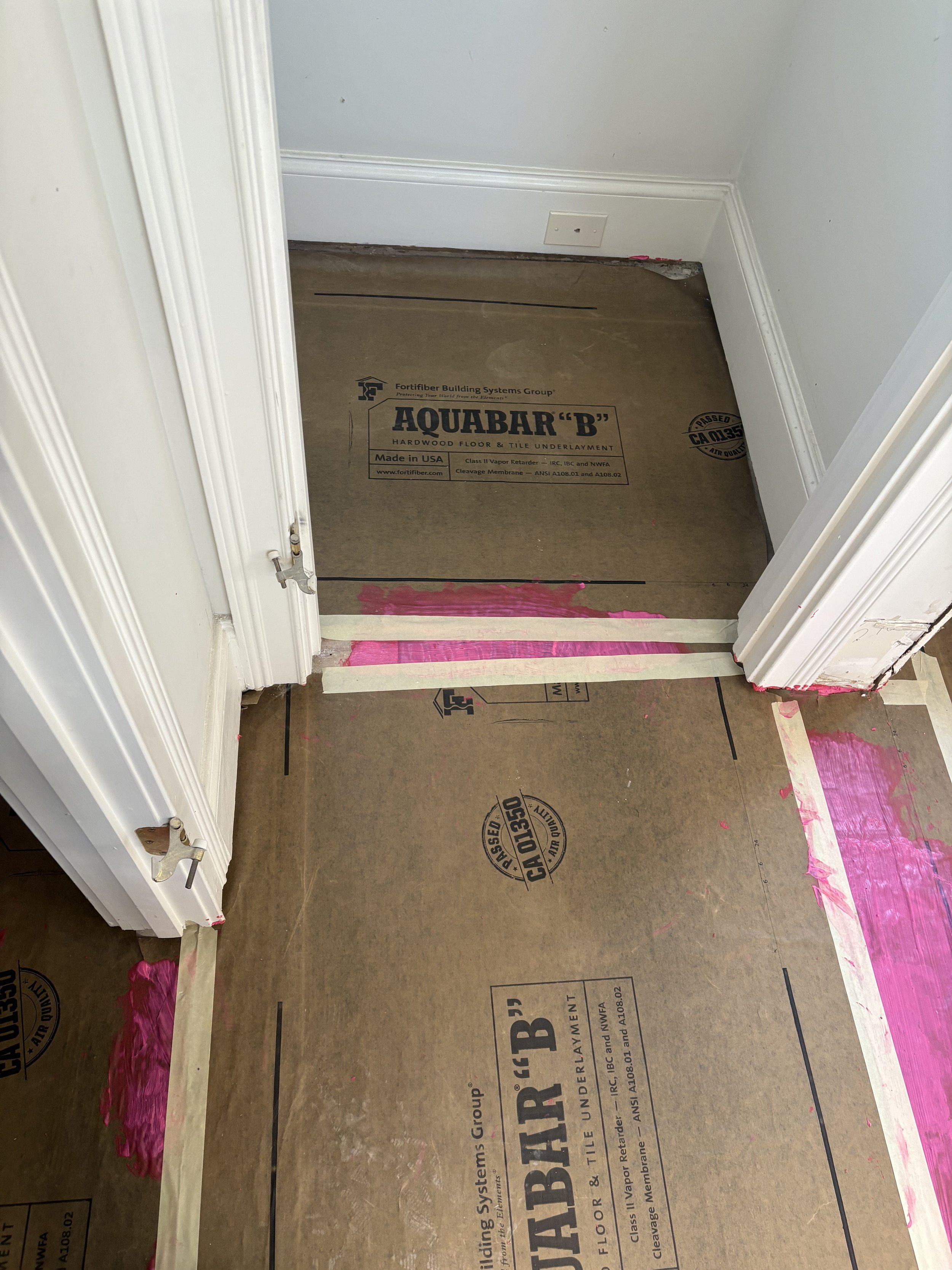 Partially completed room with subflooring and pink waterproof membrane, ready for tile installation.