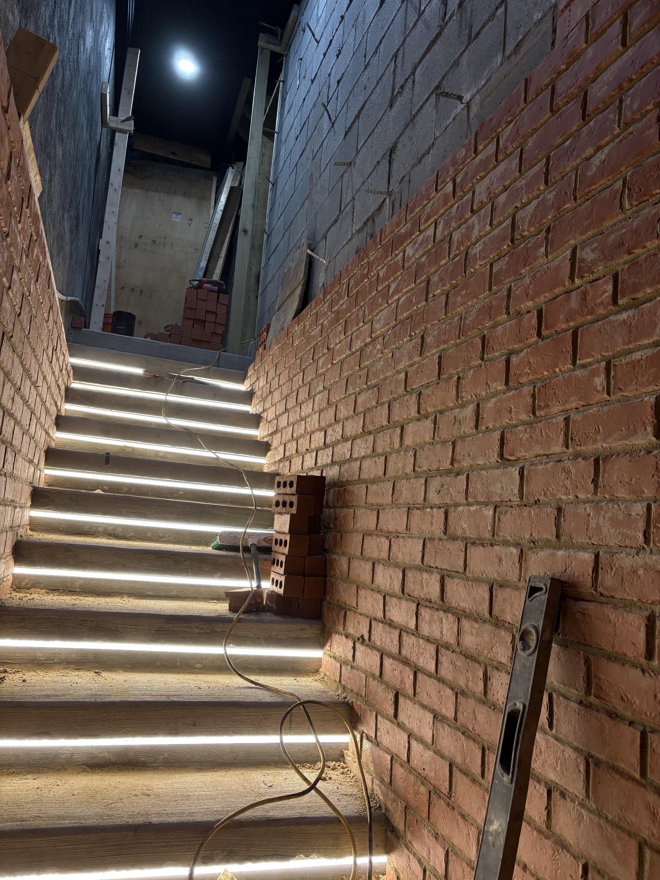 Brick staircase under construction with LED strip lights, bricks, level tool, and construction materials around.