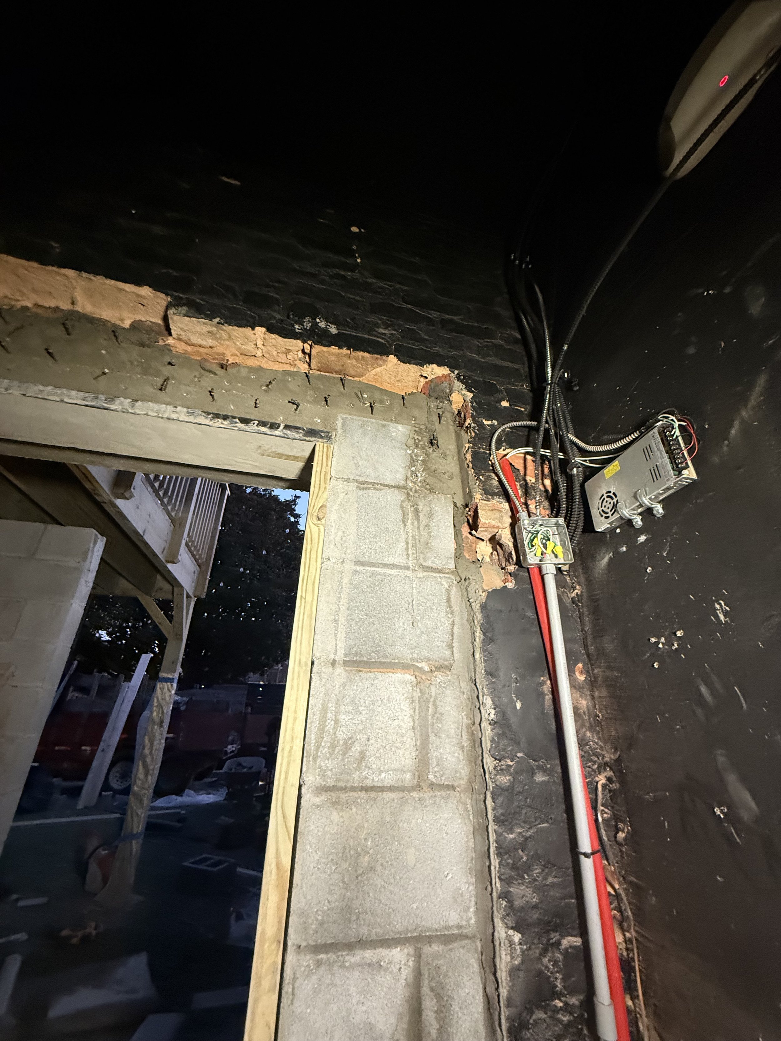 Construction or renovation work inside a building shows an unfinished window opening, with exposed brick and concrete blocks, electrical wiring, and equipment.
