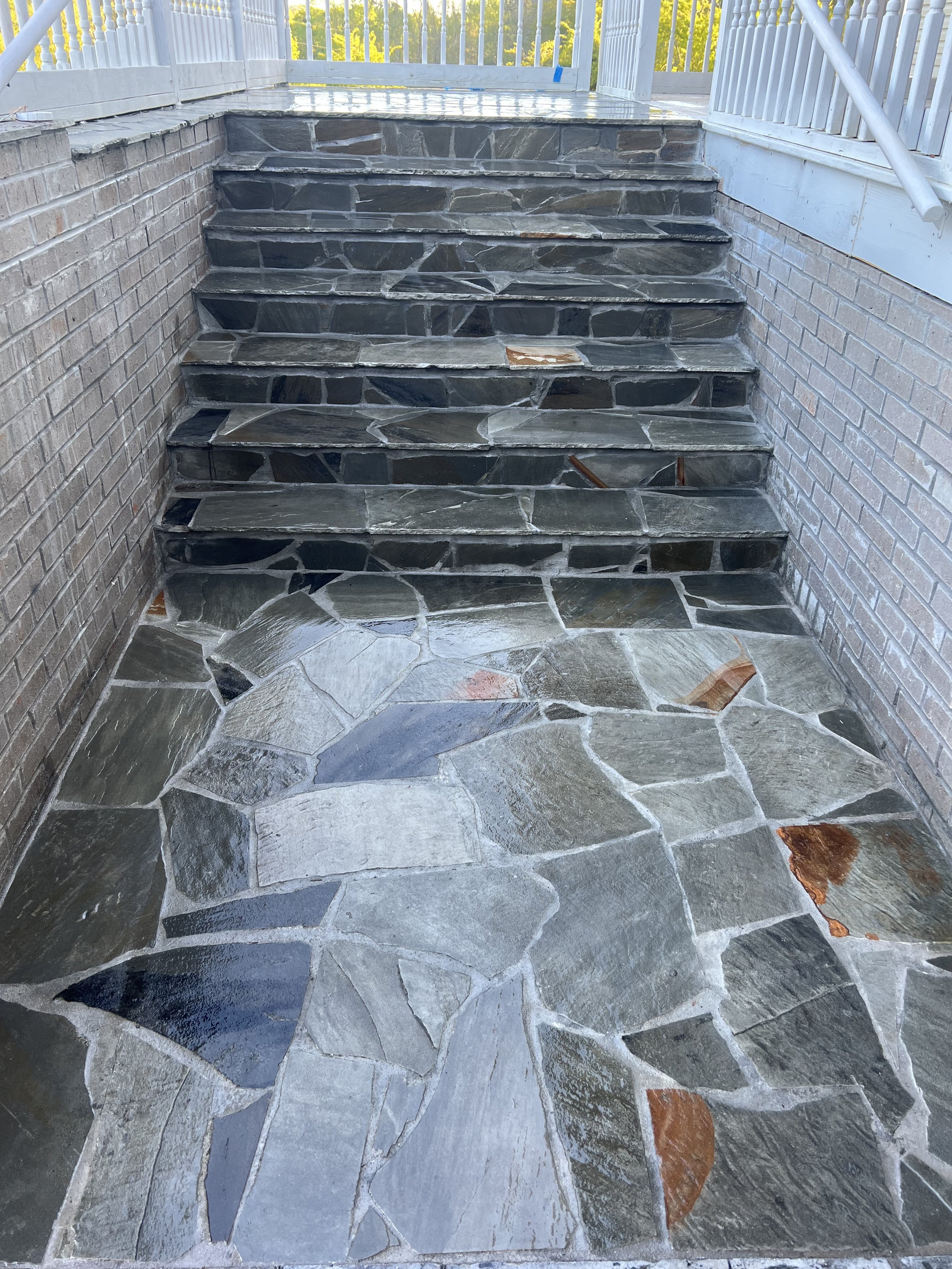 Exterior stone steps with a brick wall on each side and a white railing at the top leading to a porch or deck area.