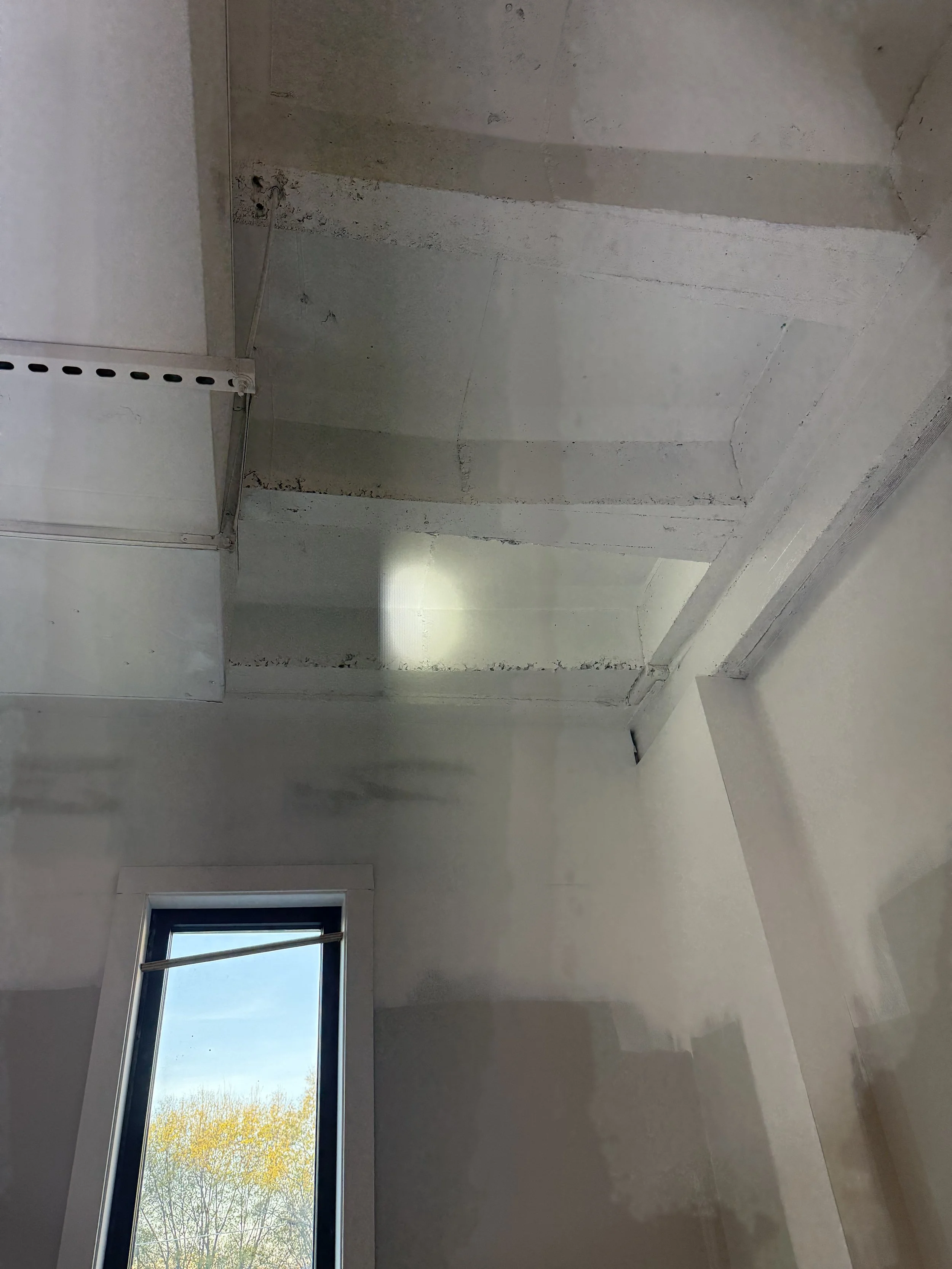 Construction room with unfinished drywall and a window showing trees outside.