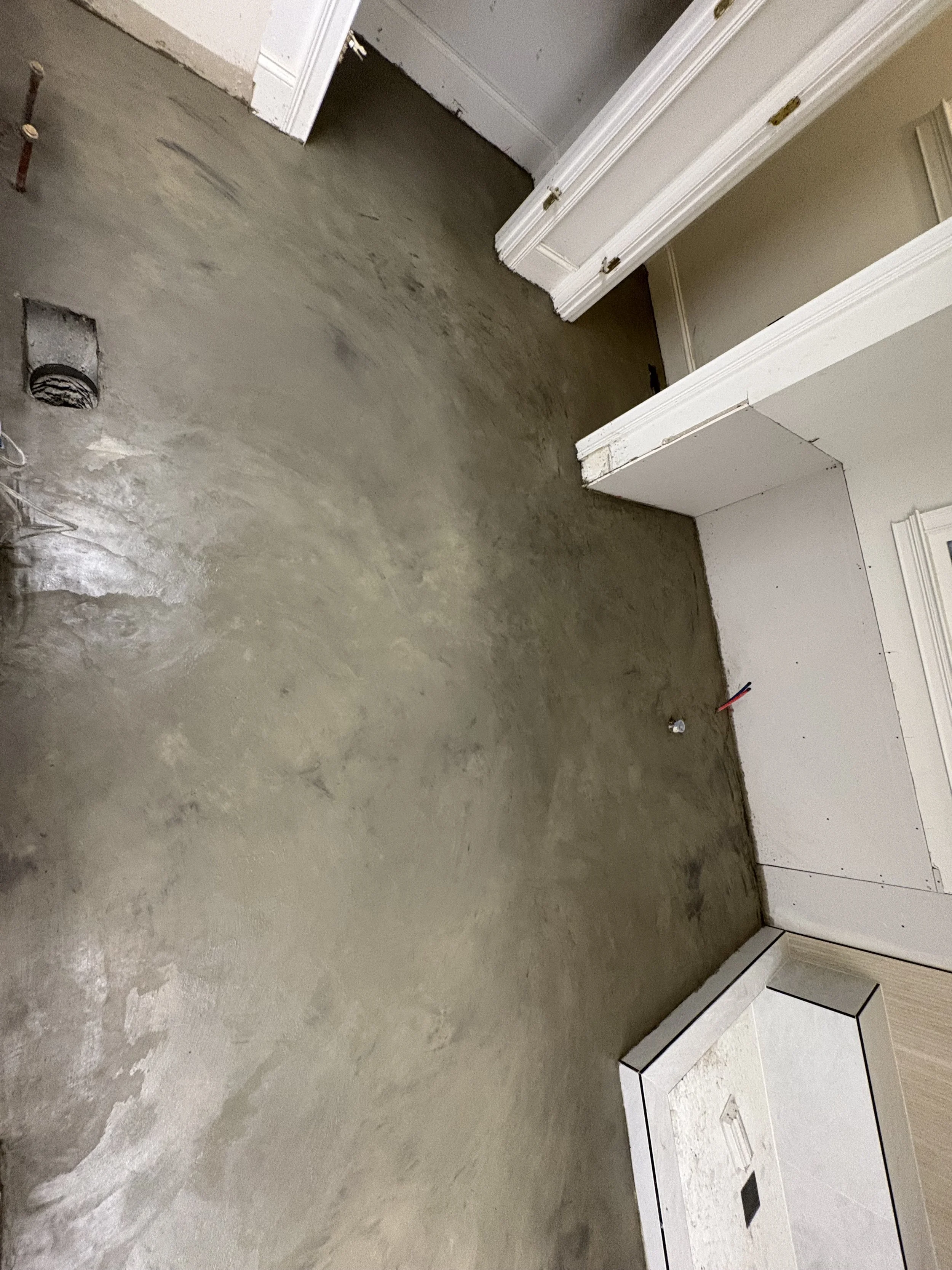 Unfinished indoor space with a concrete floor, exposed walls, and electrical wires protruding from the wall.