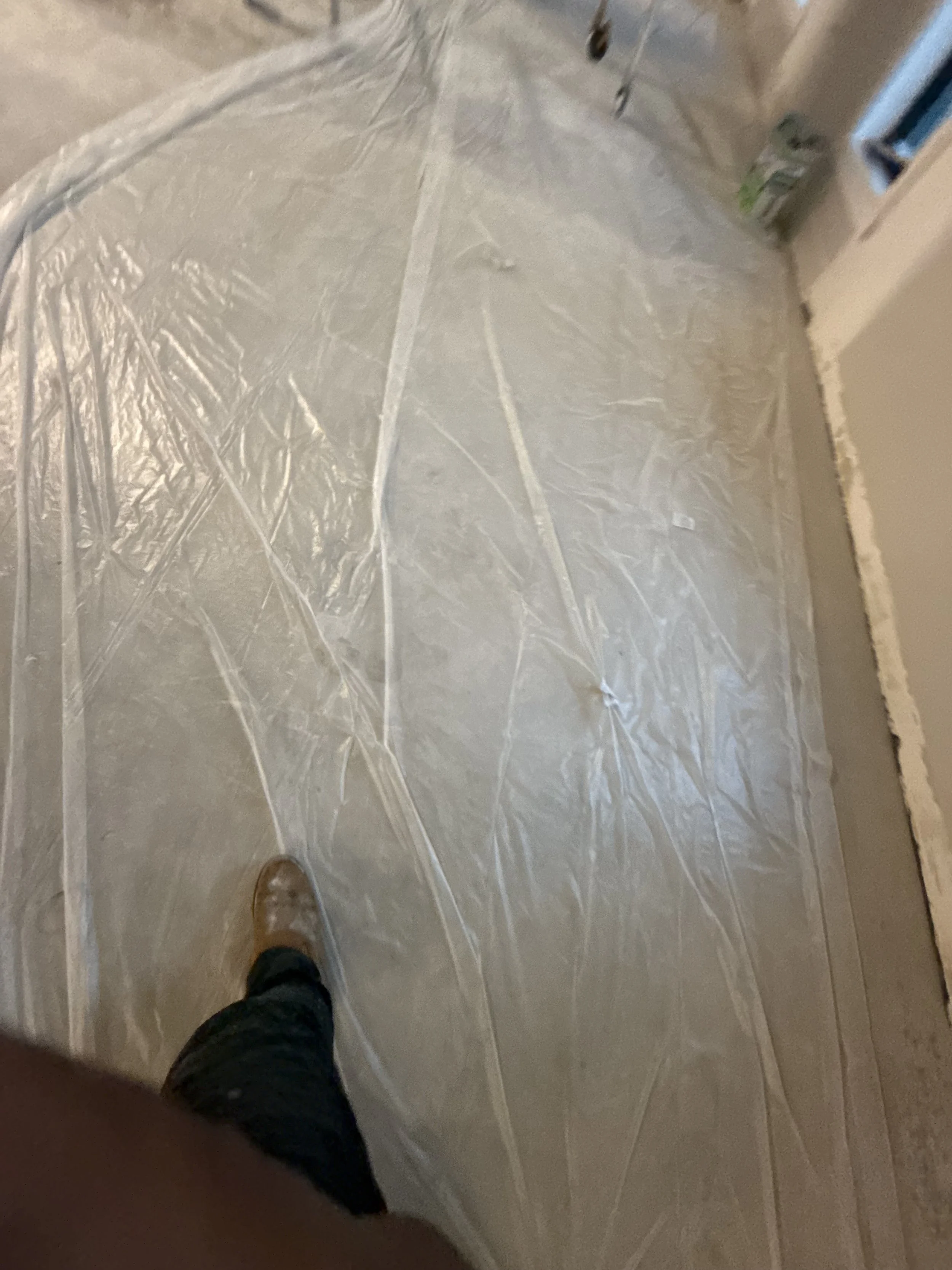 Floor covered with clear plastic protective sheet, with a person's foot visible in the lower left corner.