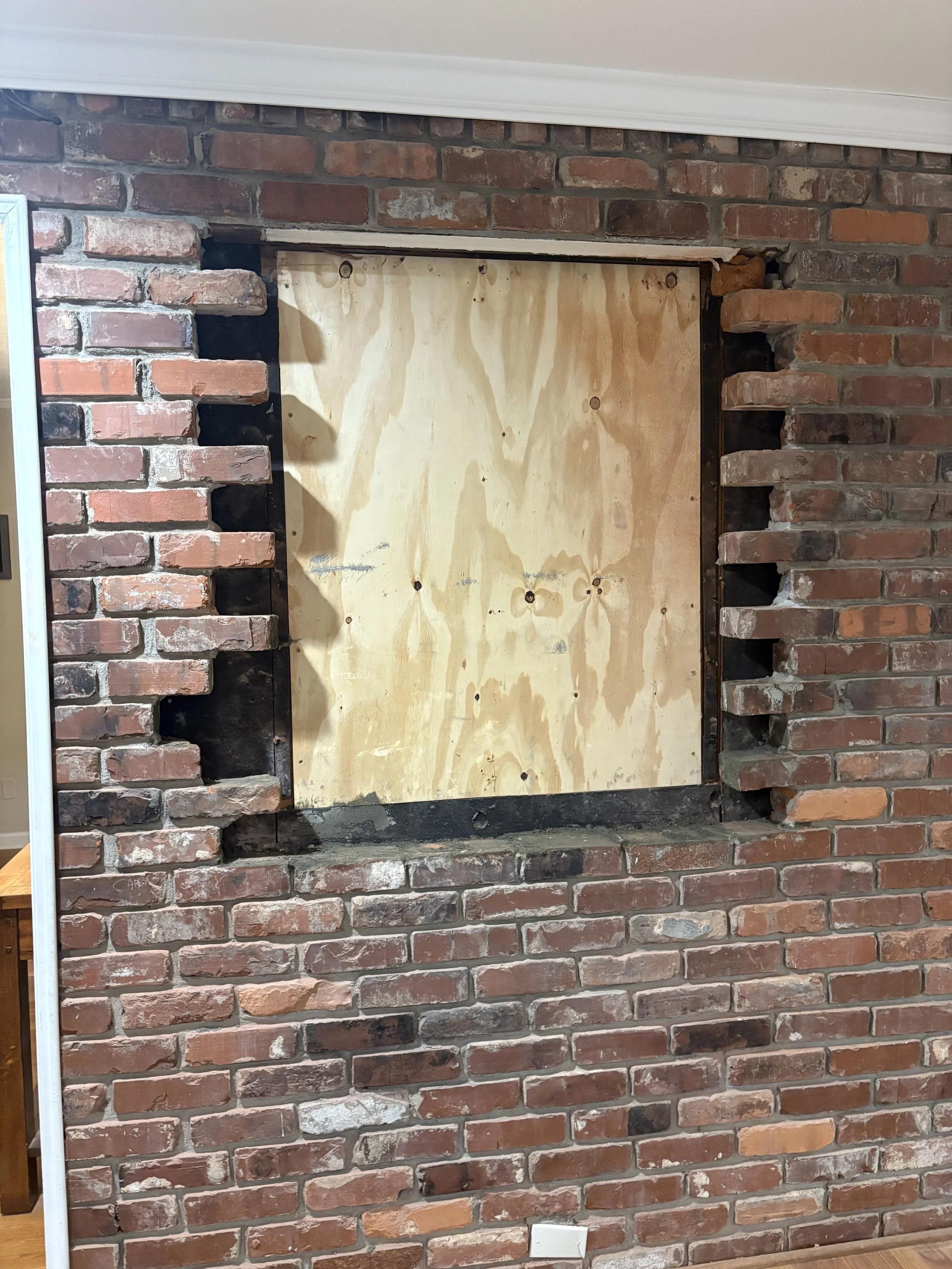 A brick fireplace with a plywood panel covering the opening.