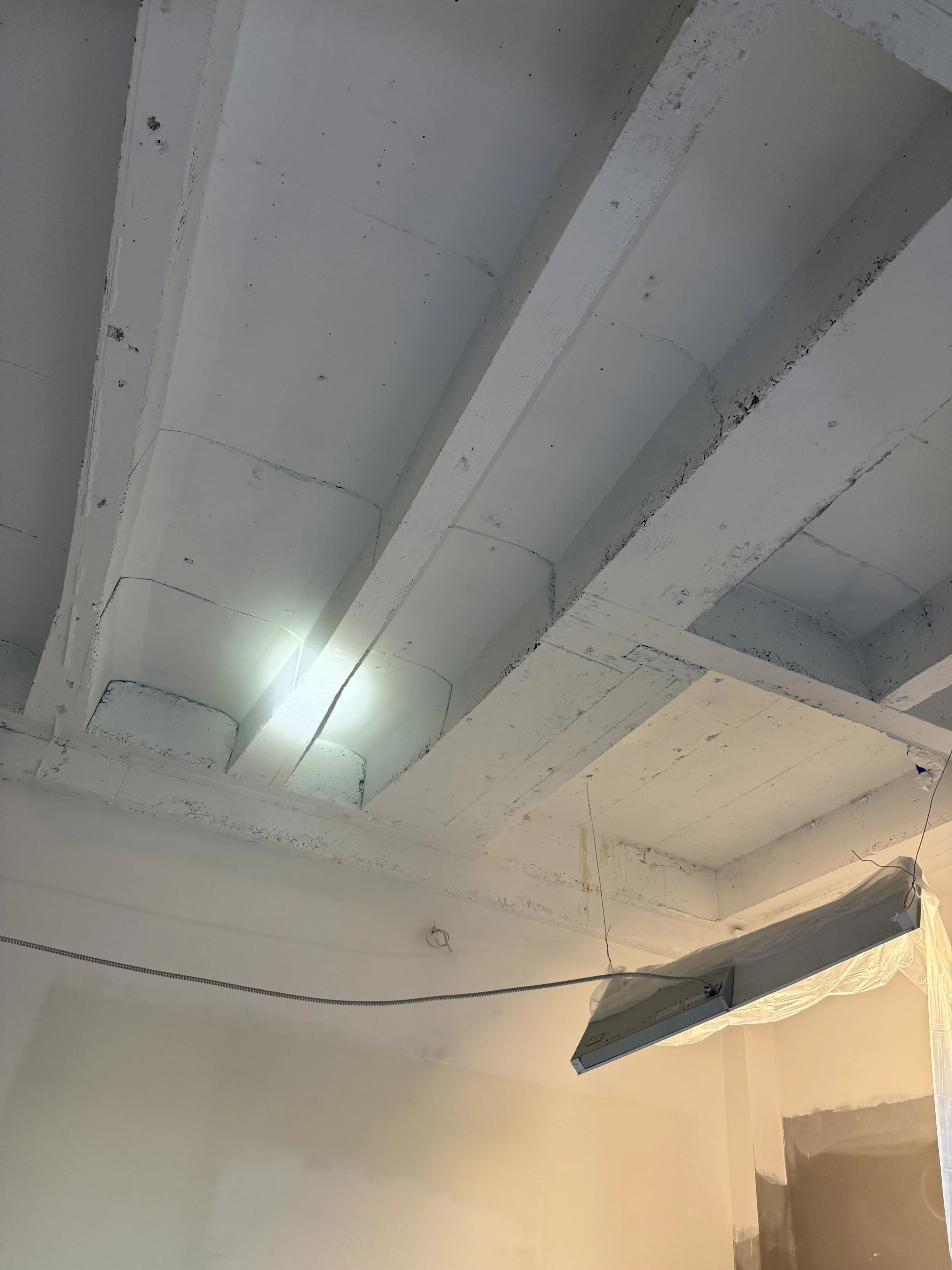 Ceiling with exposed concrete beams and a suspended lighting fixture in a room under construction or renovation.
