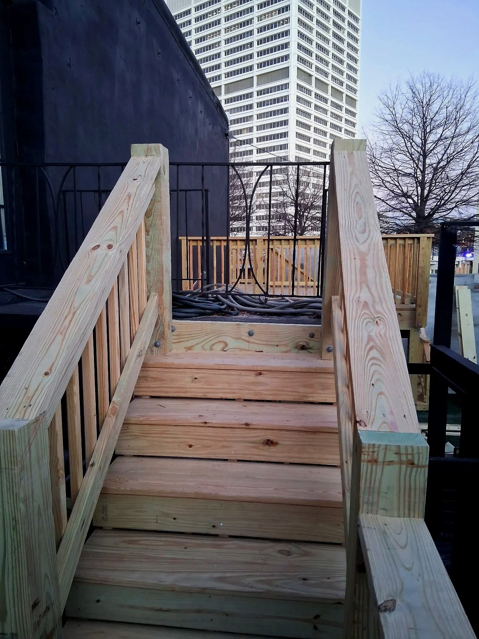 Wooden stairs with railing leading to a rooftop deck under construction, with a city skyline in the background.