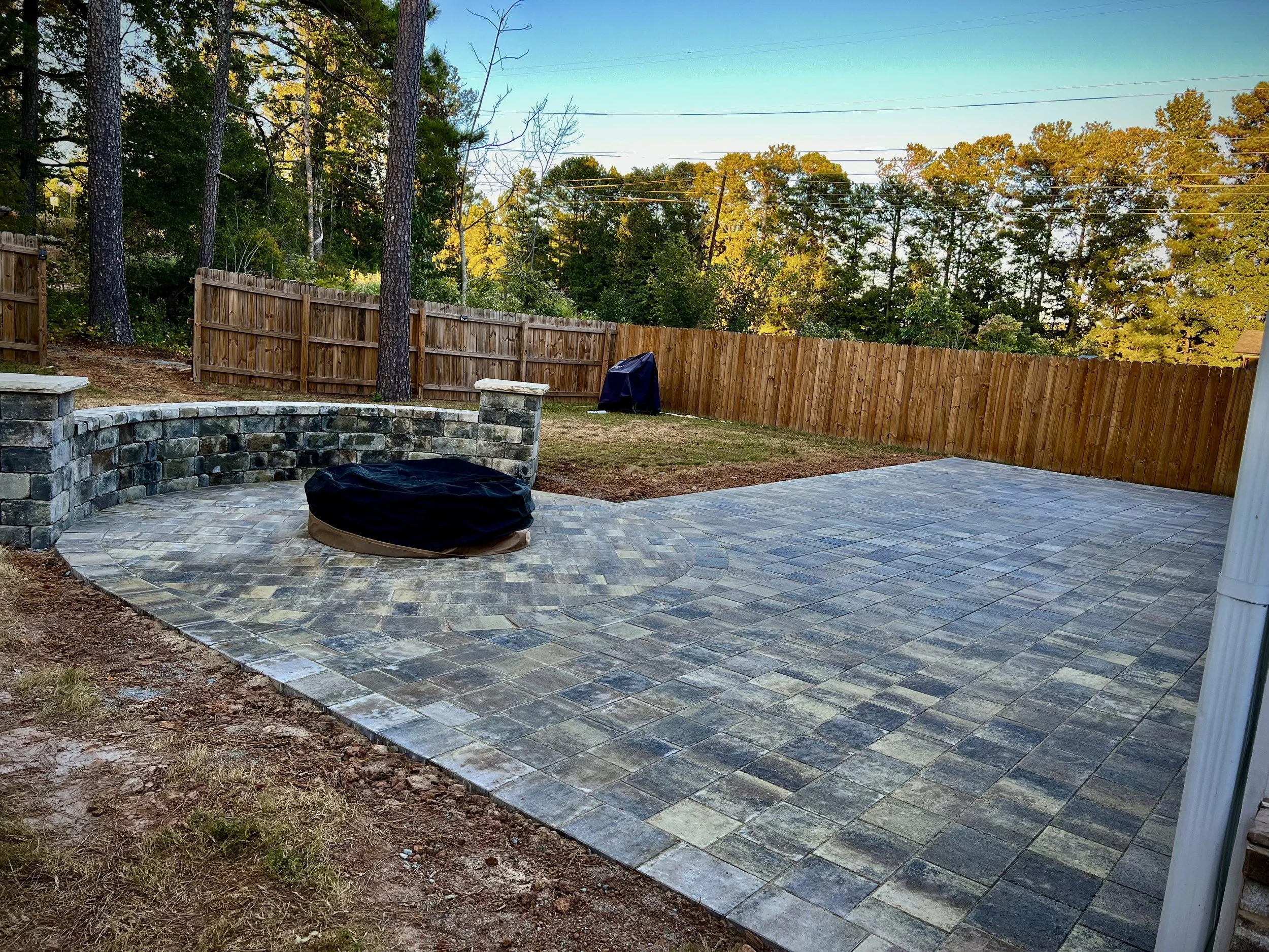Backyard with newly built paver patio, wooden privacy fence, and trees in the background during daytime.