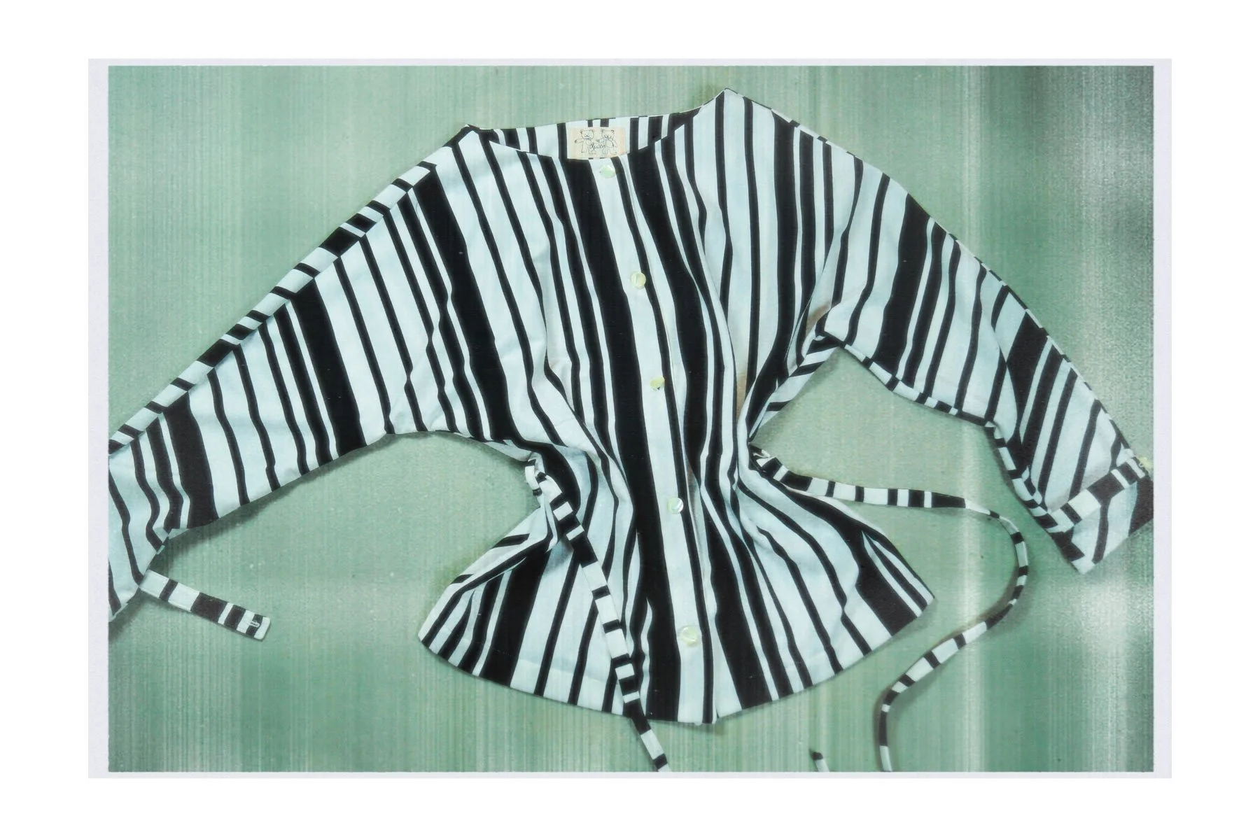 A black and white vertically striped long-sleeve button-up shirt with a tie around the waist, laid flat on a green textured surface.