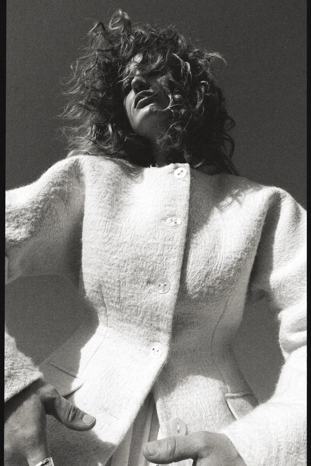 A woman with curly hair wearing a textured cardigan with buttons, posing against a dark background.