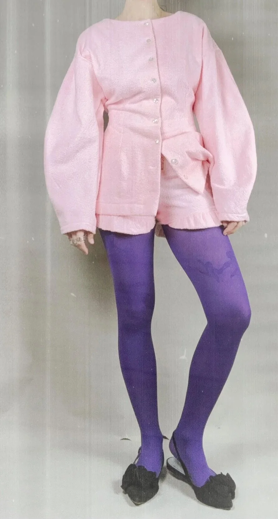 Fashion mannequin wearing a pink button-up jacket, pink shorts, purple tights, and black shoes with decorative bows.