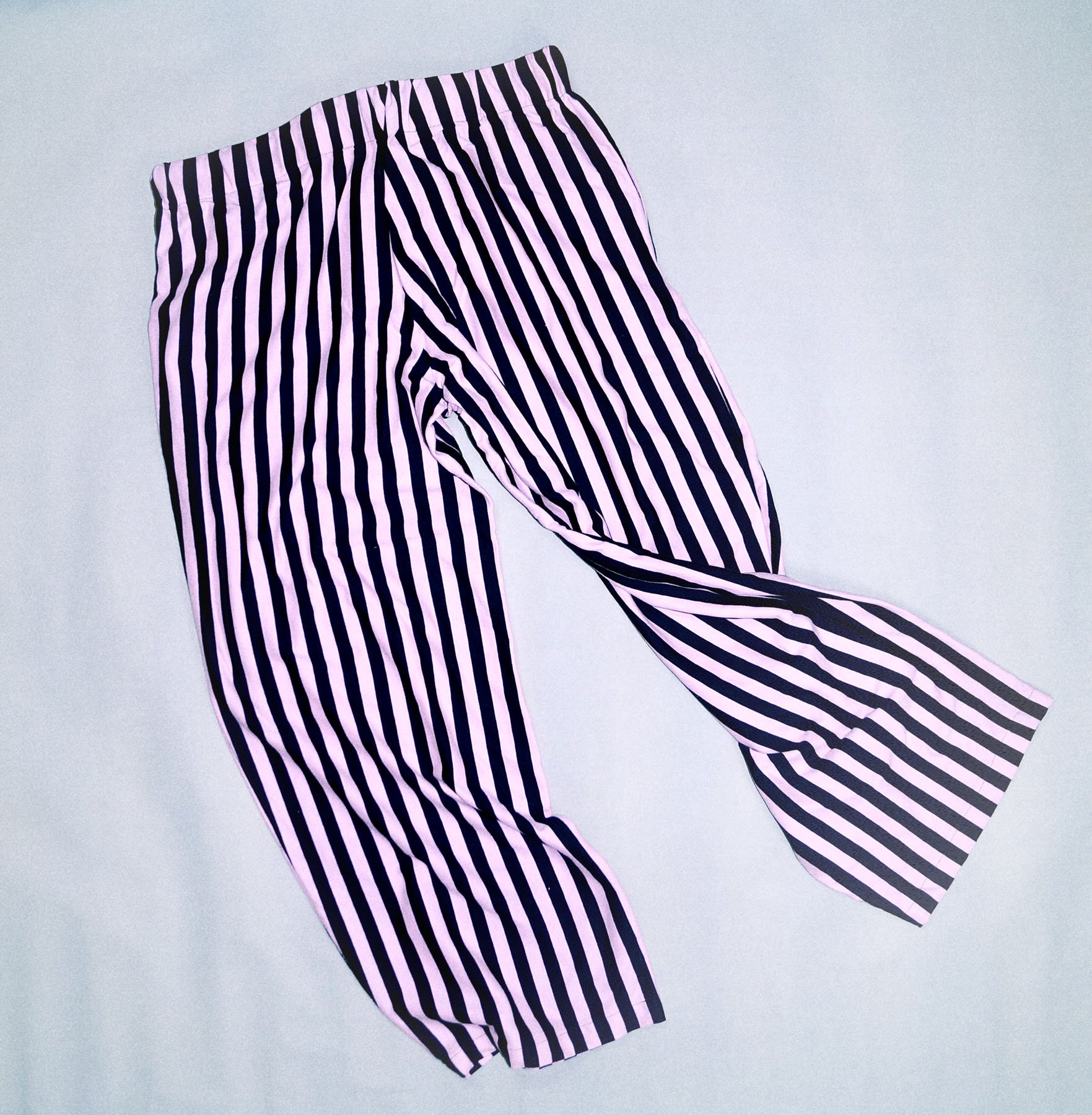 Pair of pink and black striped pants laid on a light gray surface.