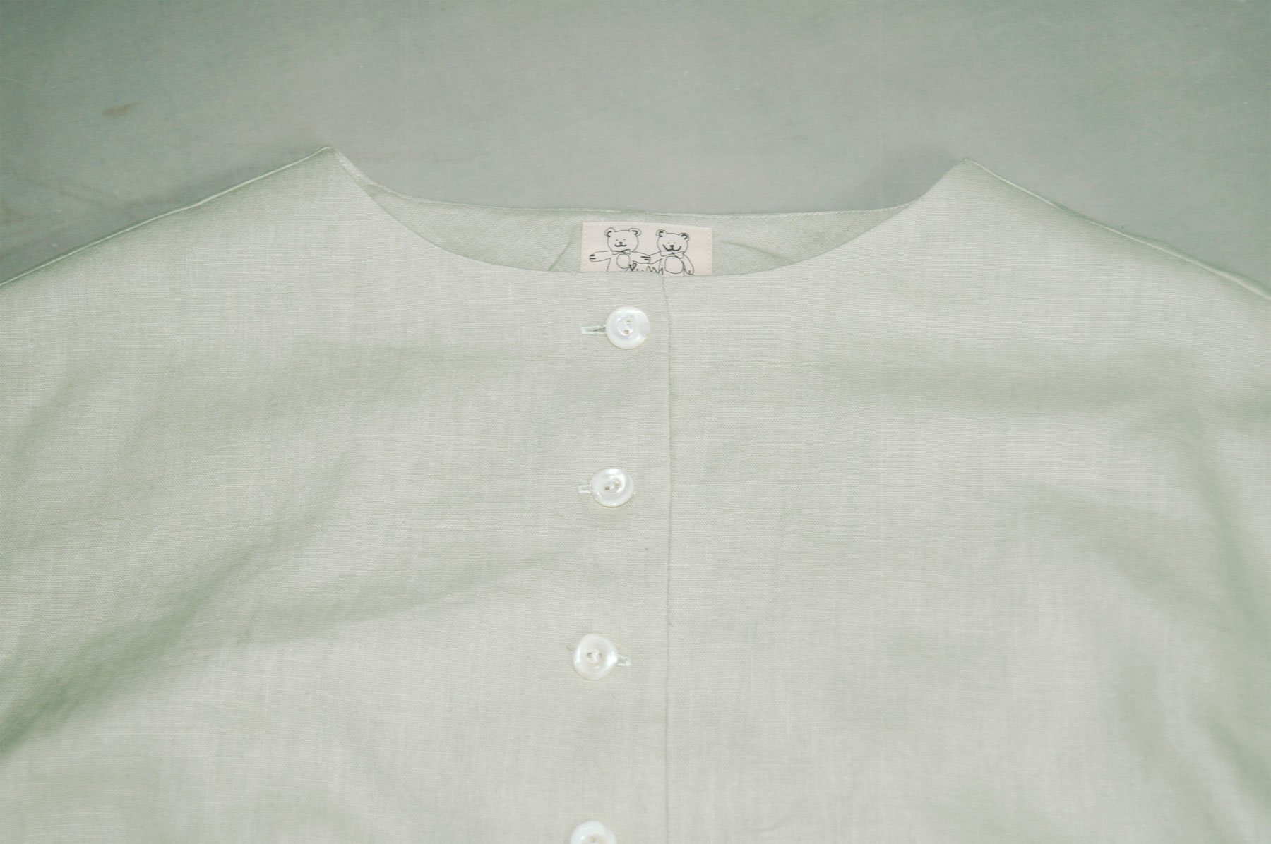 Close-up of a light-colored shirt with a small teddy bear graphic on the tag, featuring two teddy bears holding hands.