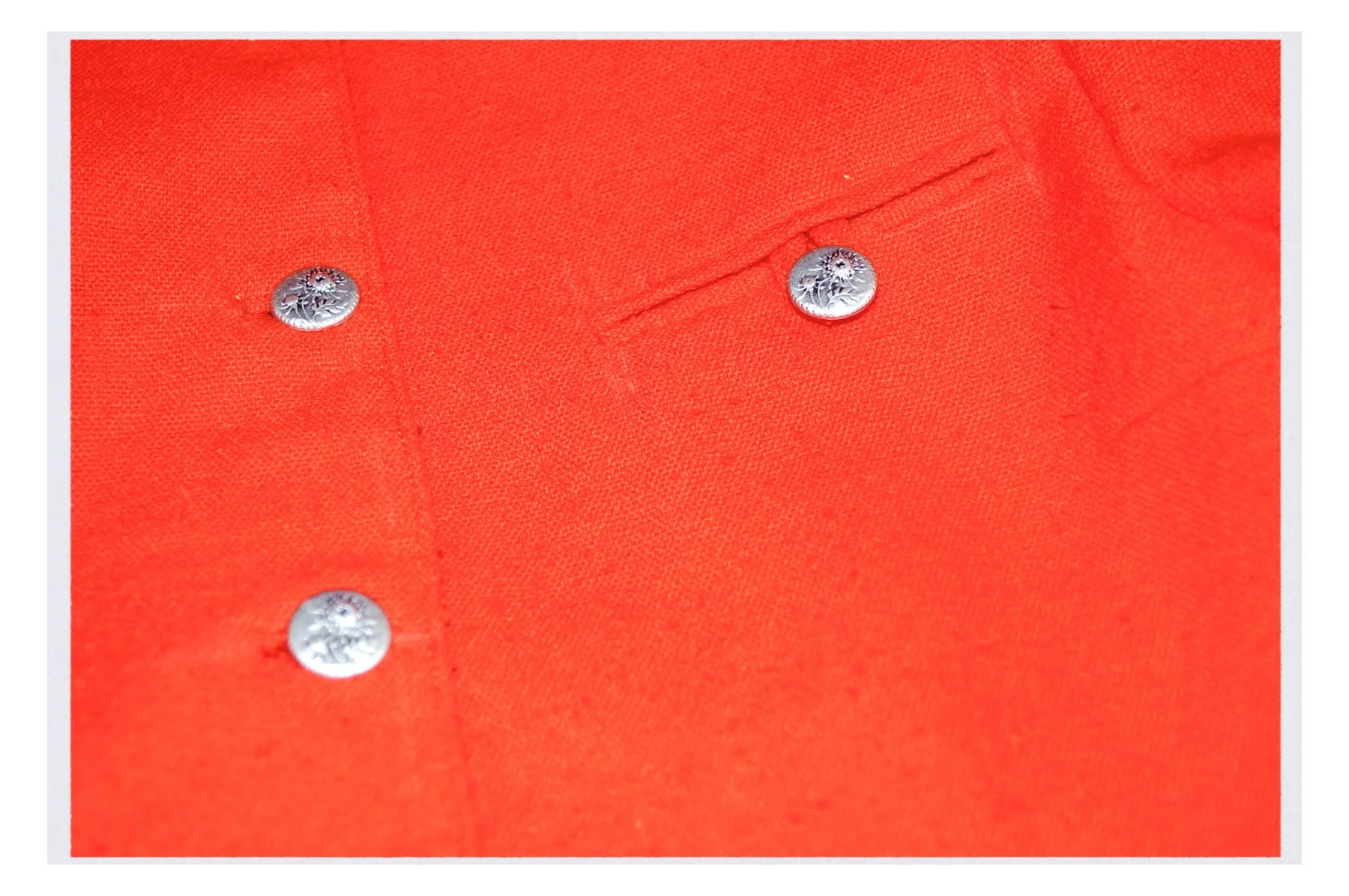 Close-up of a bright orange fabric with metal buttons, likely part of a shirt or jacket.