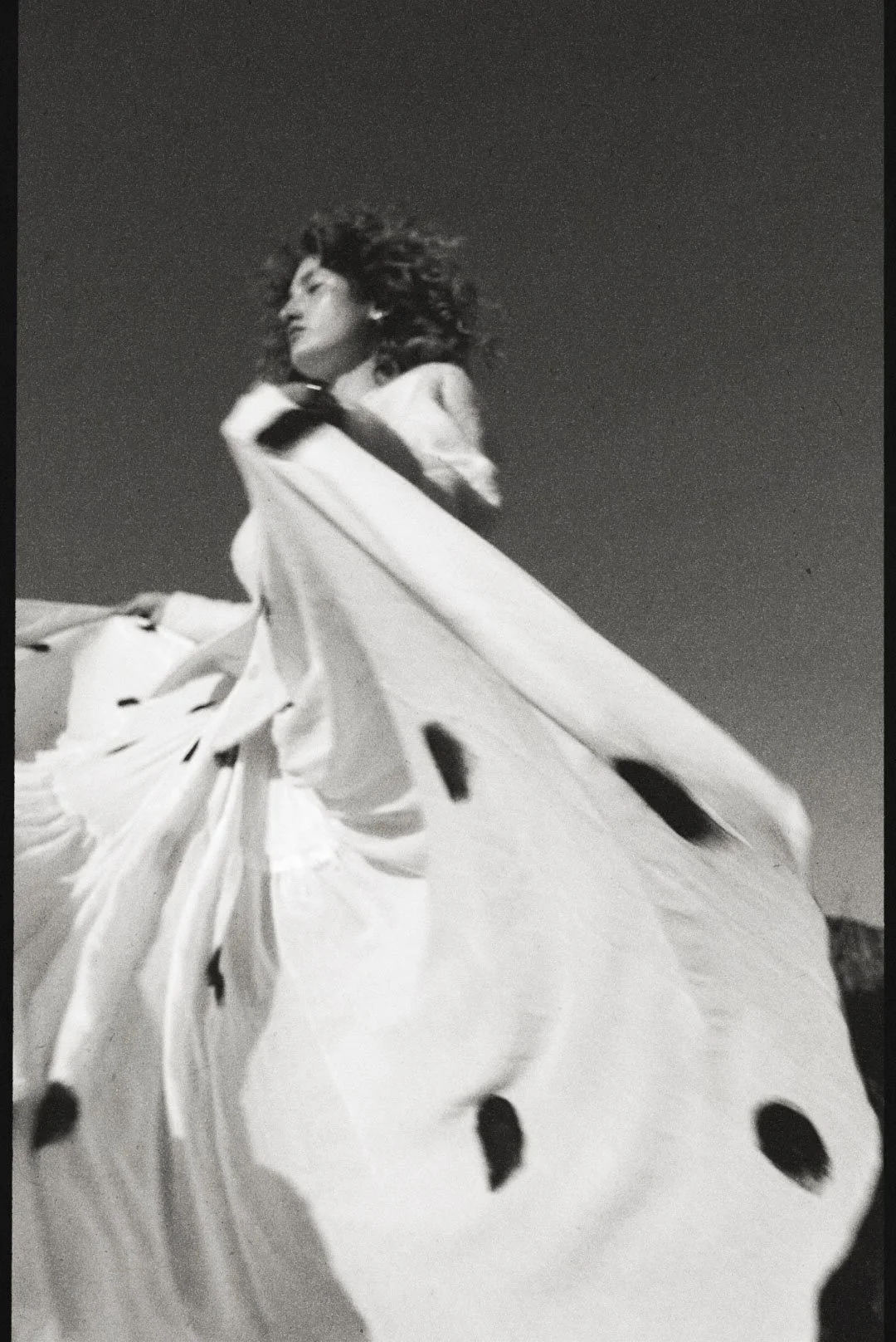 A woman with curly hair wearing a white dress and large butterfly wings with black spots.