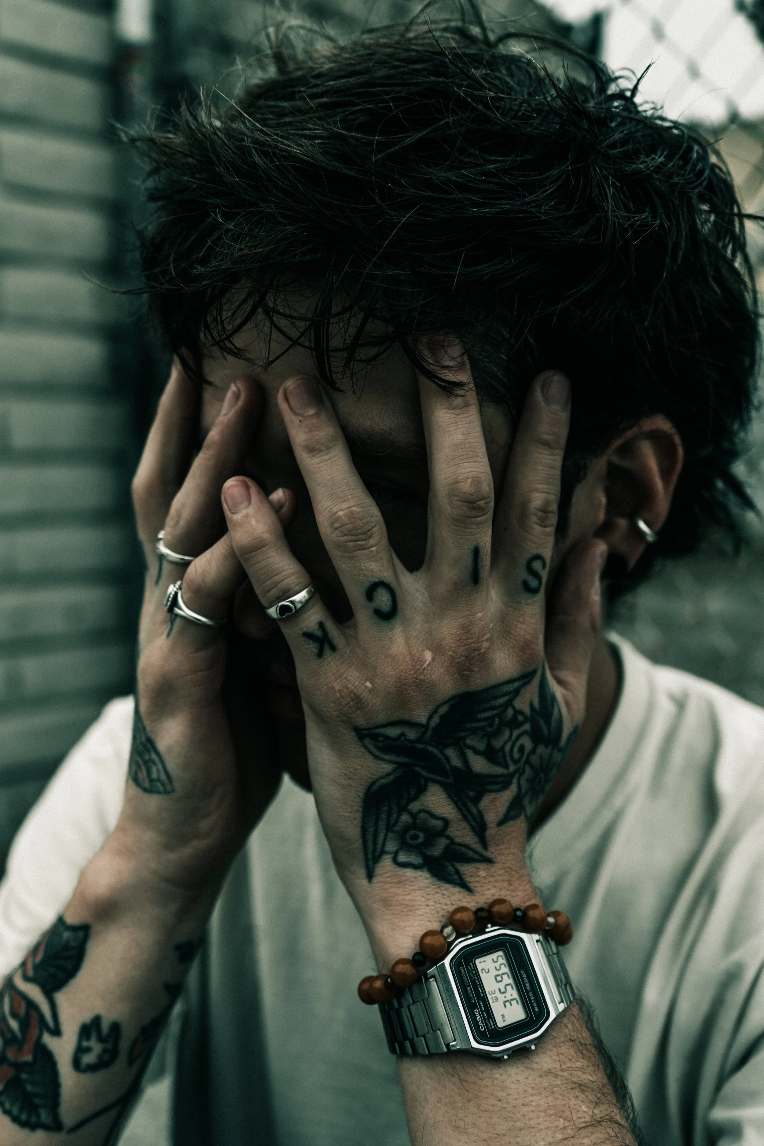 tattooed person covering face with hands, moody cinematic portrait with soft natural light and gritty tones