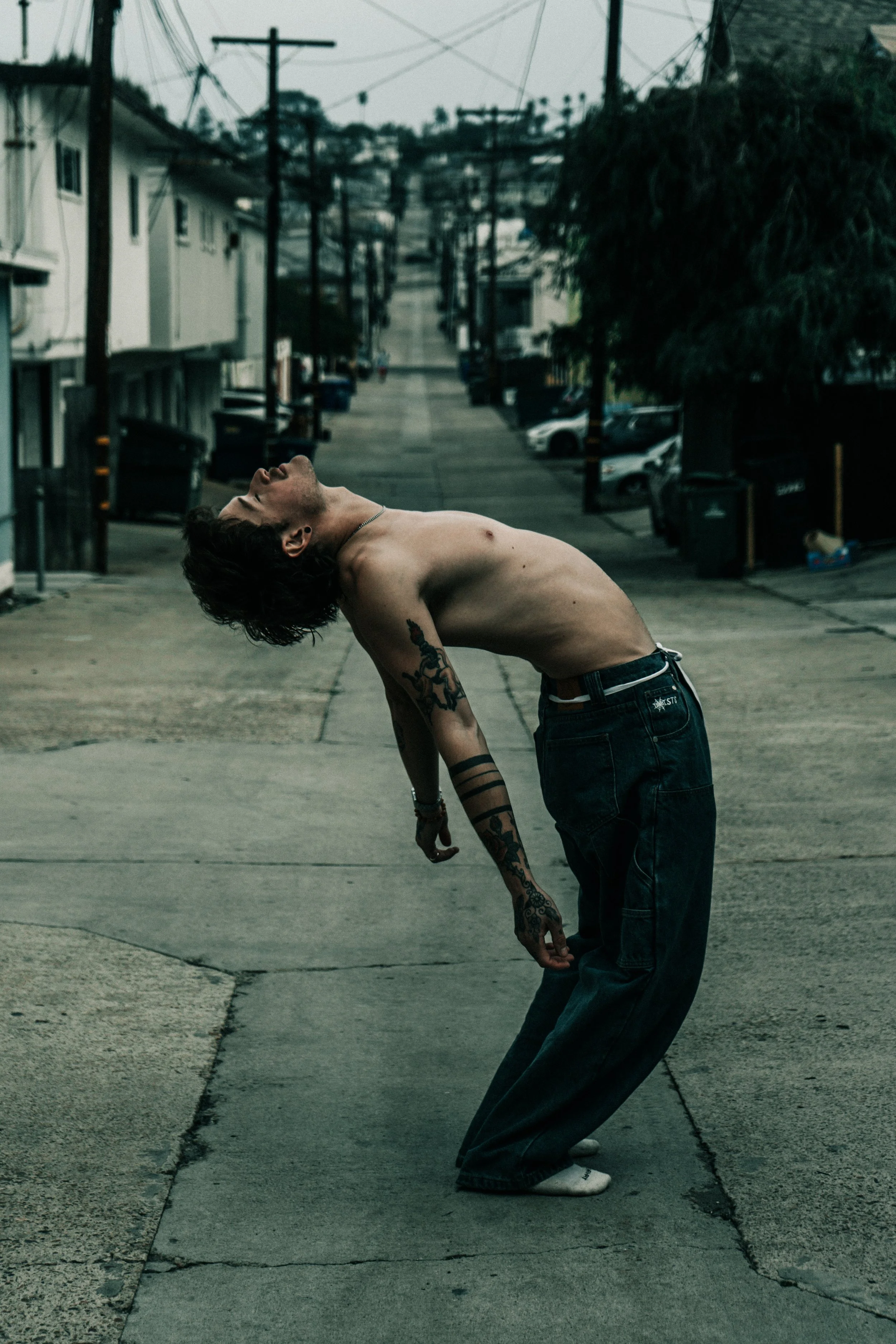 shirtless model arching back in an empty alleyway, dramatic cinematic portrait with urban environment