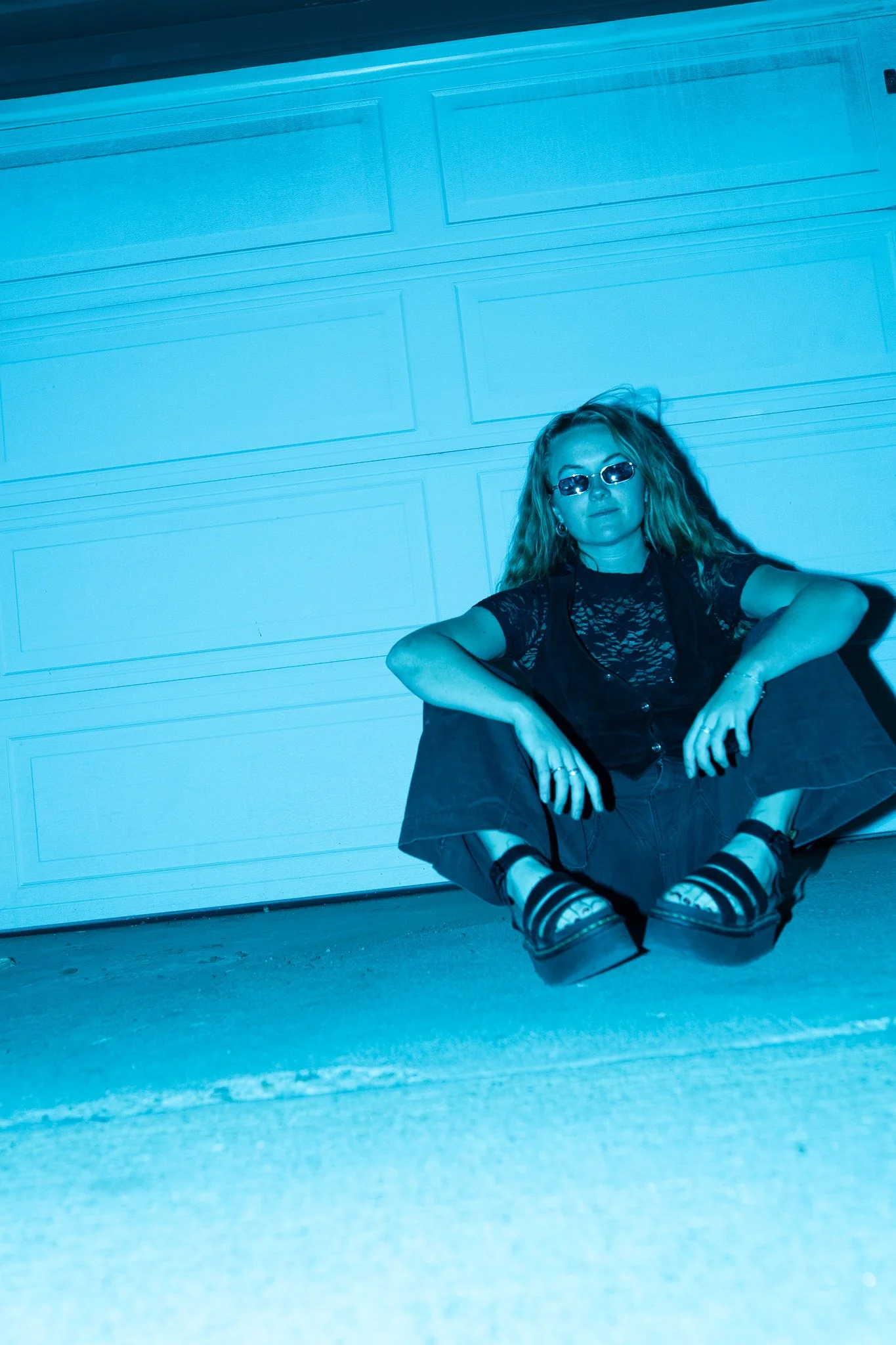 blue lit portrait of a woman sitting on ground in garage, cinematic fashion photography with direct flash