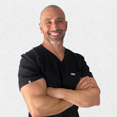 Dr. Aaron Sakevich in black scrubs, with arms crossed against a light background.