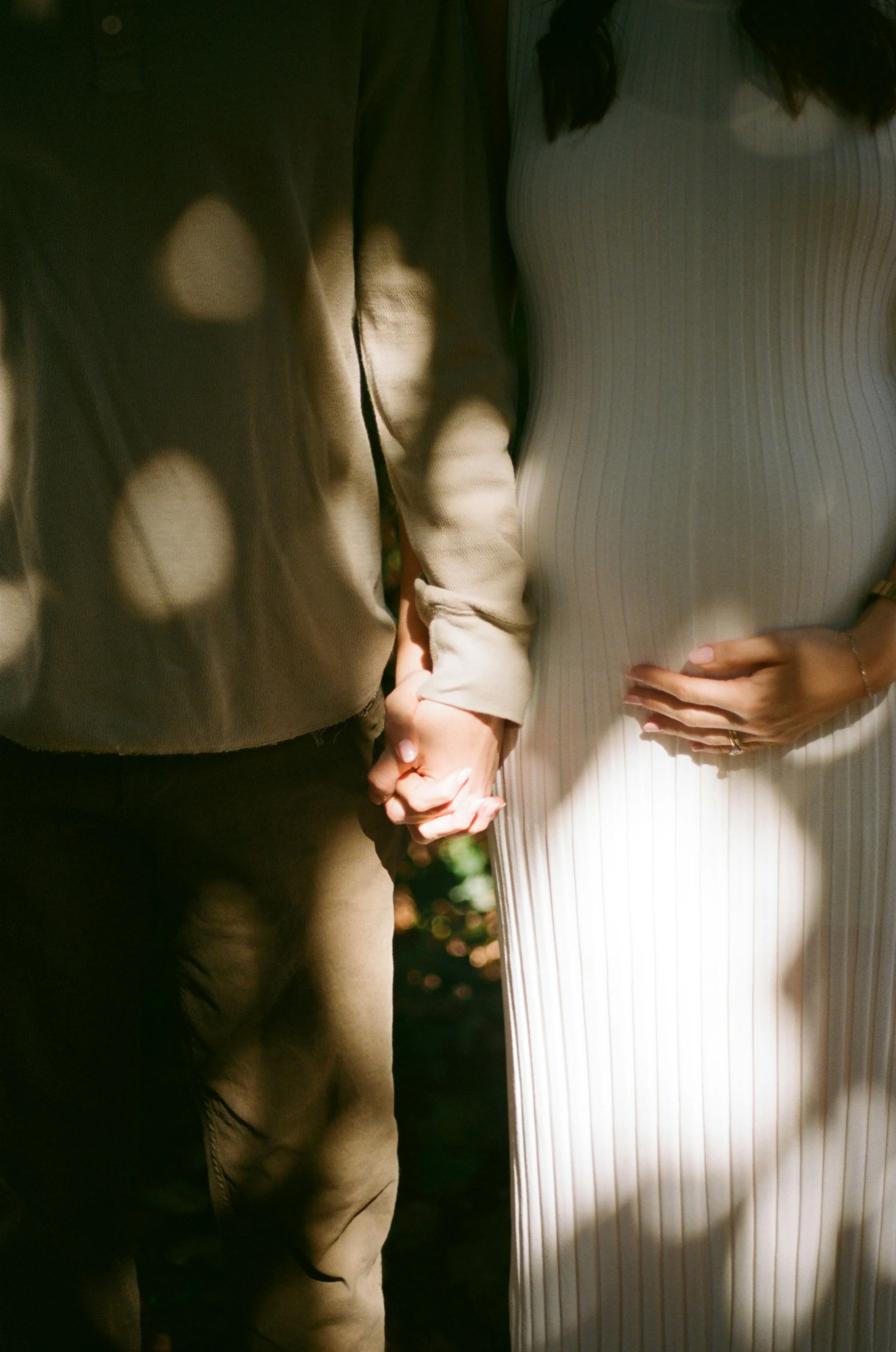 close up of couple holding hands with the pregnant woman also holding her belly