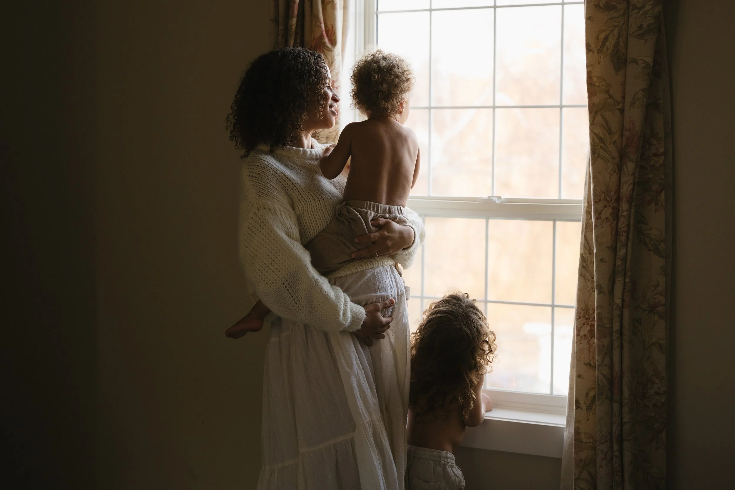 mom and two young children looking out the window mom holding younger child