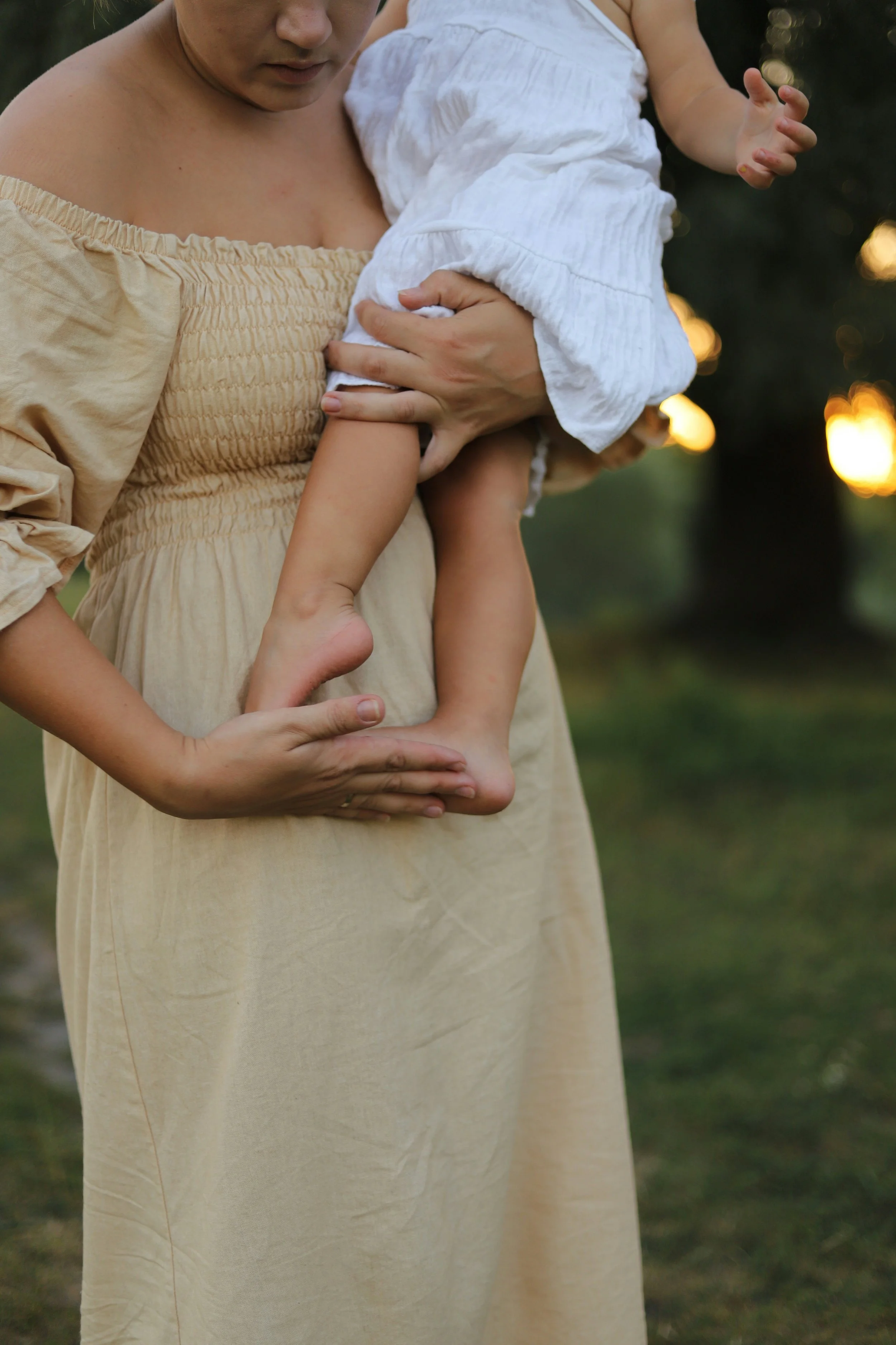 mom holding toddler outside and has hands resting on child's feet