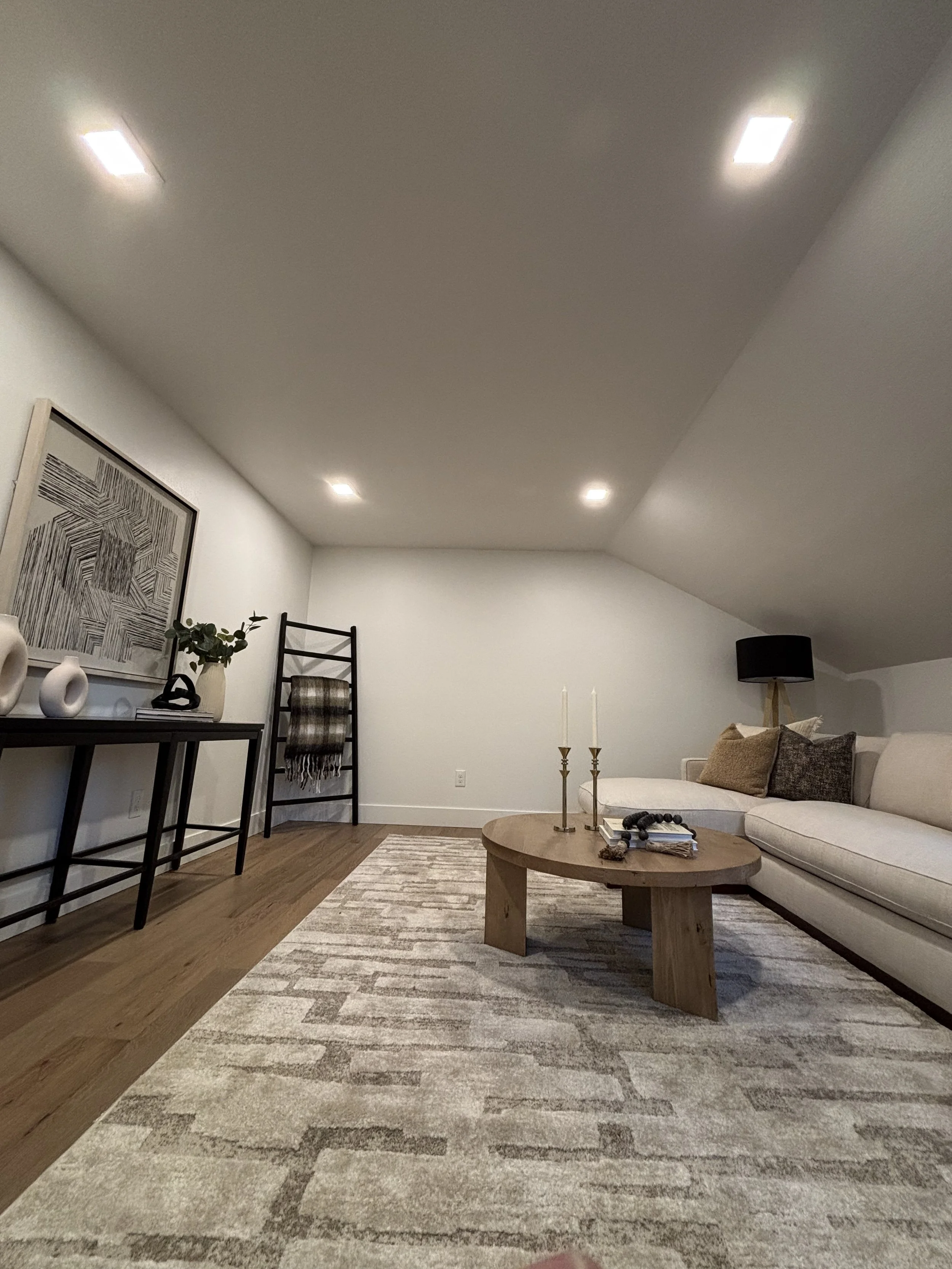 Living room with white couch, wooden coffee table, black table with white vases, wall art, and a black floor lamp.