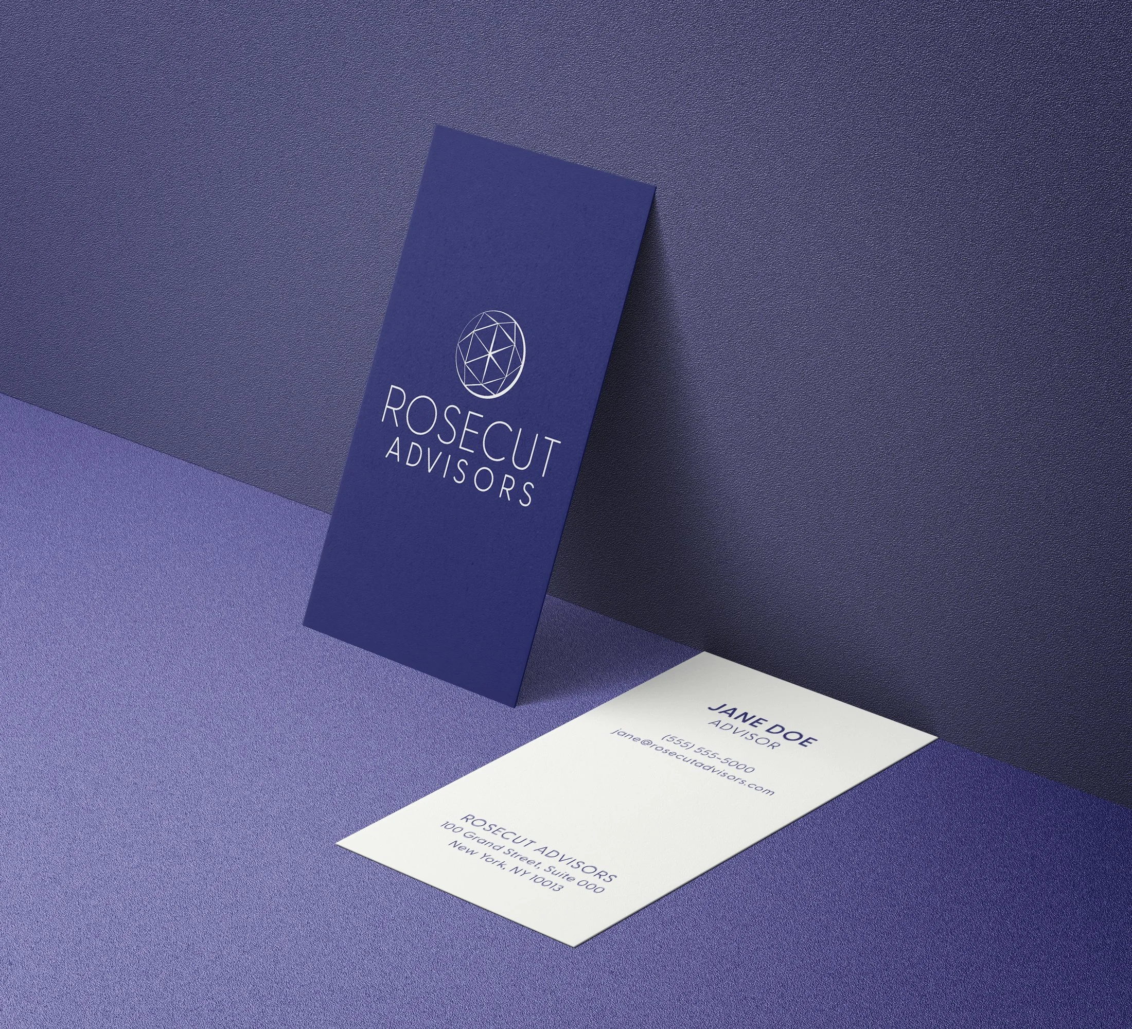 Business card and folded brochure for Rosecut Advisors on a purple surface with a textured background. The business card is white with blue text, showing contact information for Jane Doe, an advisor. The brochure is navy blue with a geometric logo an