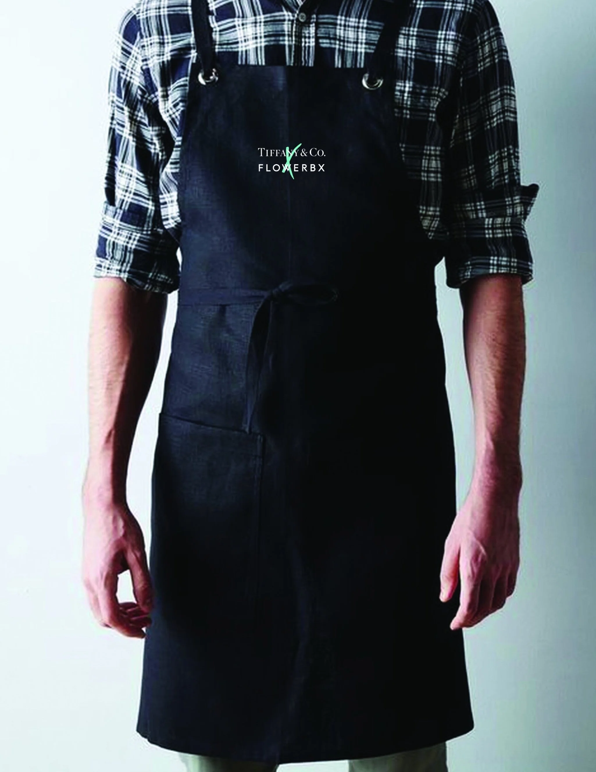 Person wearing a black apron with Tiffany & Co. and Flowerbx logos over a plaid shirt.