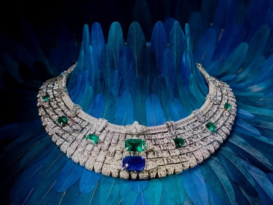 A diamond and emerald necklace placed on blue feathers.