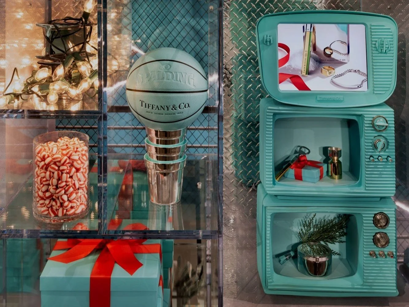 Display of Christmas decor with teal jewelry boxes, a Tiffany & Co. basketball-shaped trophy, a glass jar of peppermint candies, and holiday-themed jewelry and gifts.