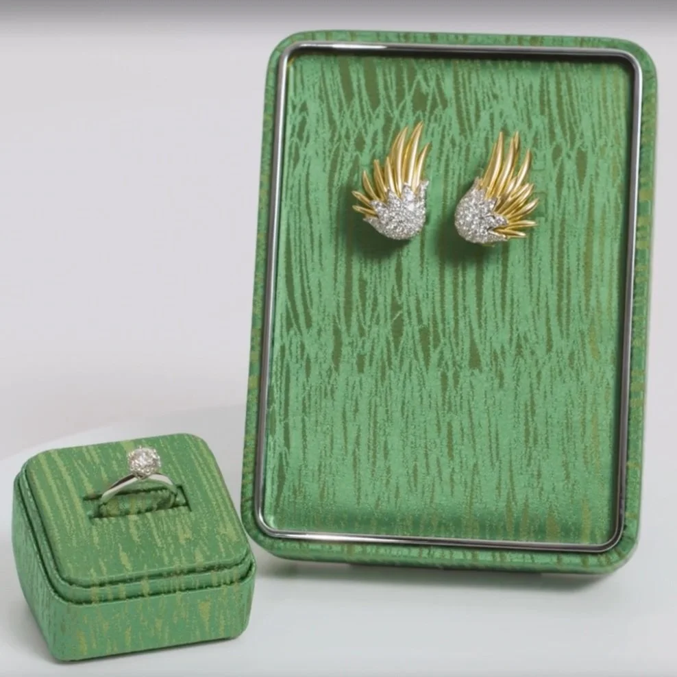 A jewelry display with a pair of gold and diamond earrings on a green textured board, and a ring with a large diamond in a matching green box.