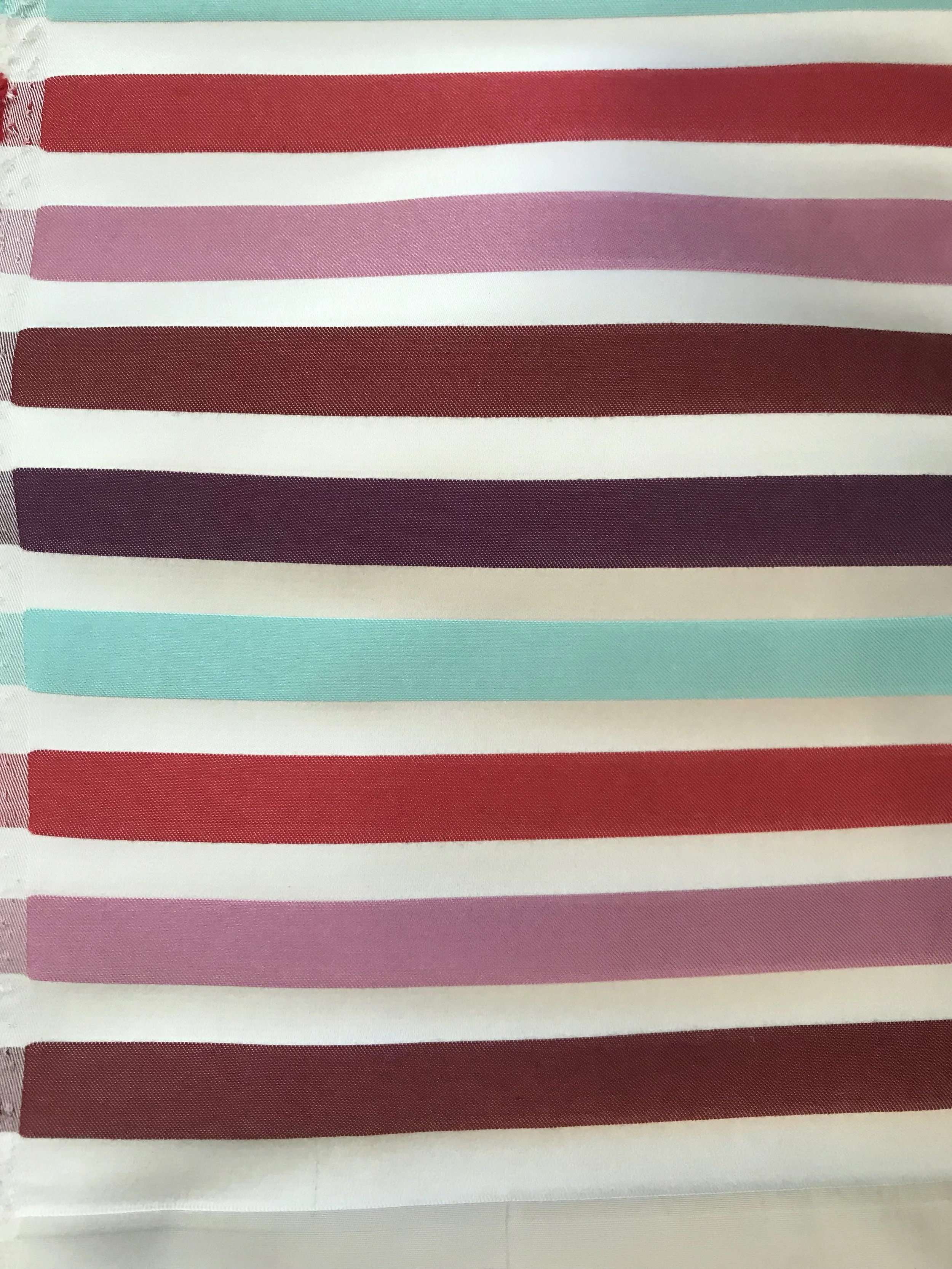 Close-up of fabric with horizontal stripes in shades of pink, purple, red, light blue, and white.