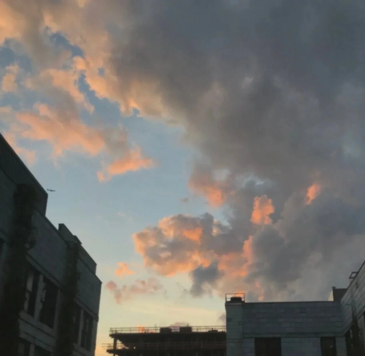 Sky with pink and gray clouds above city buildings at sunset.