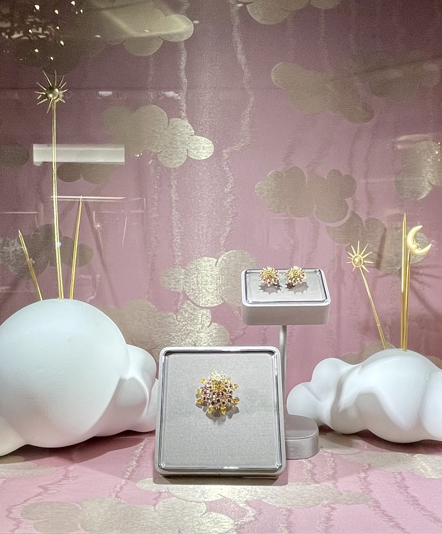 Display of jewelry featuring star and moon motifs, set against a pink and gold cloud-patterned background with decorative clouds, gold rods, and cloud figures.