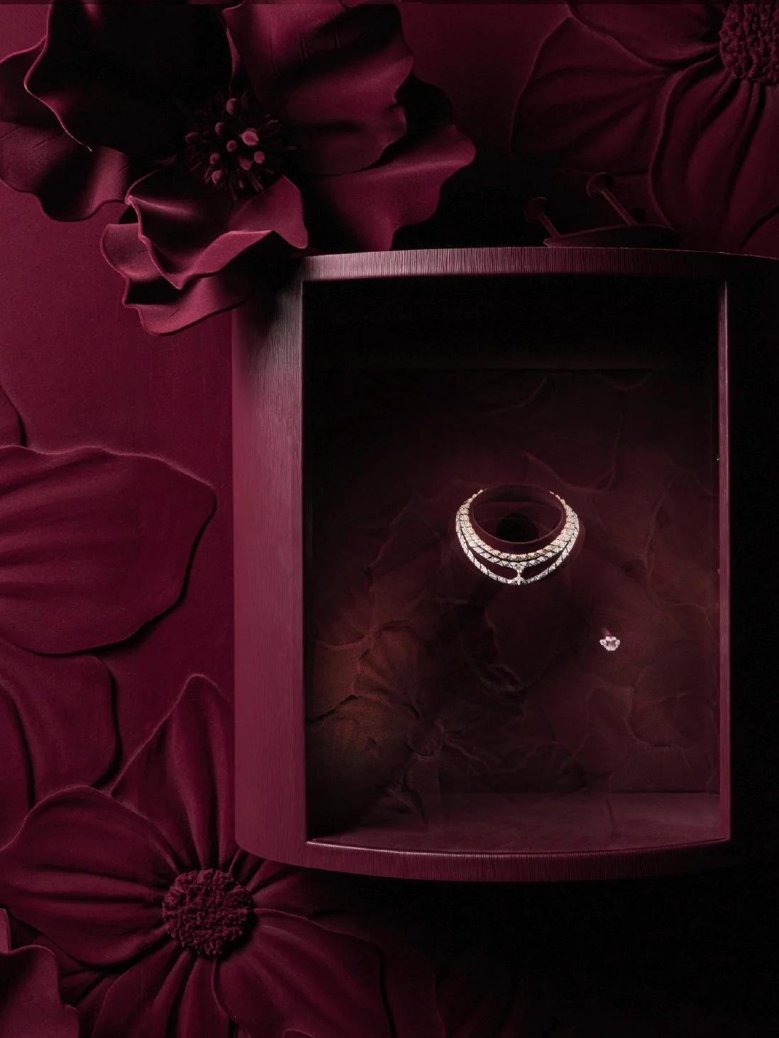 A jewelry box with a diamond ring inside, placed on a dark burgundy fabric background with floral patterns.