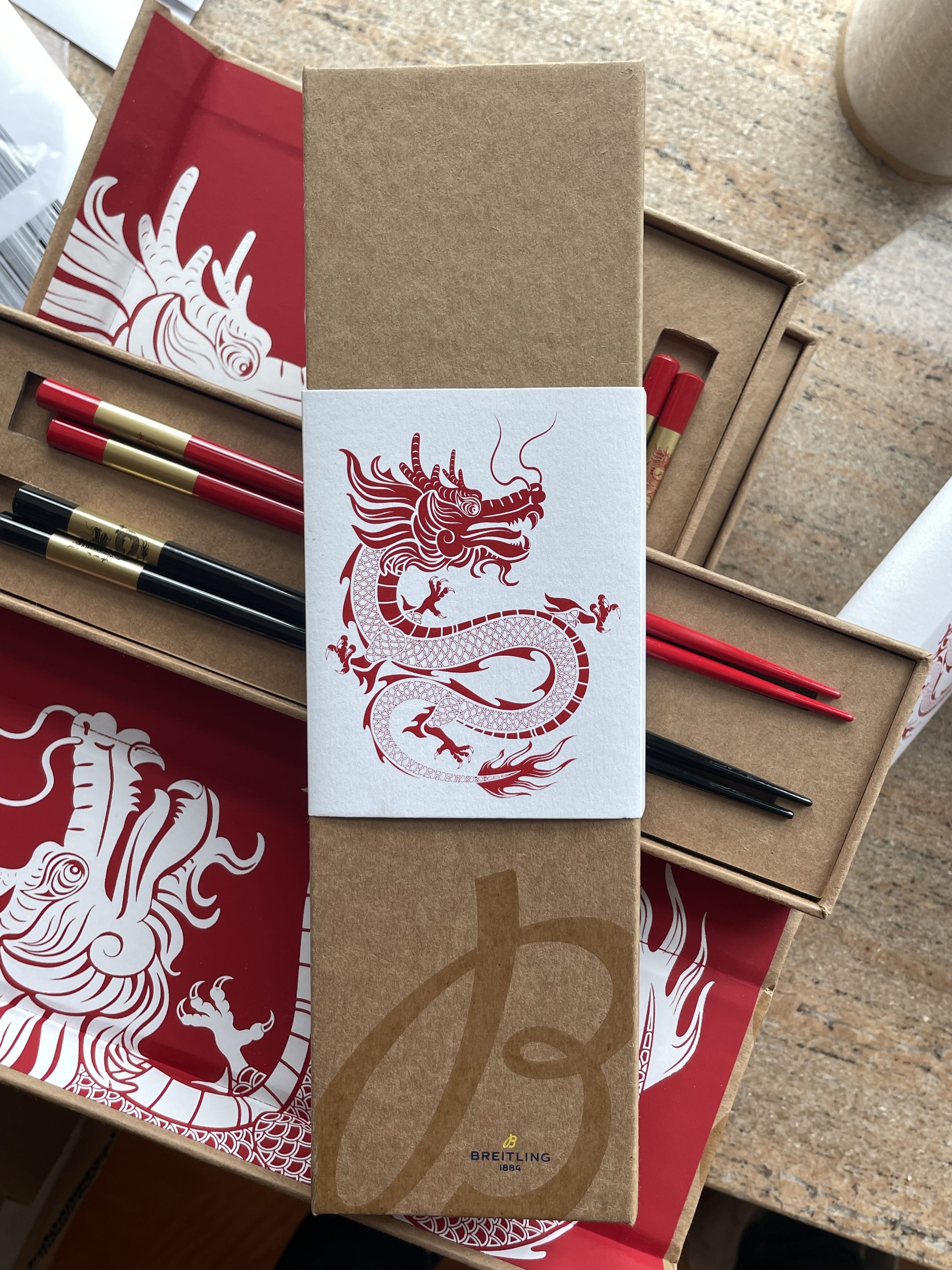 A box of pens and markers with a sticker featuring a red dragon illustration, along with packaging that has a large Chinese character and the Breitling logo.