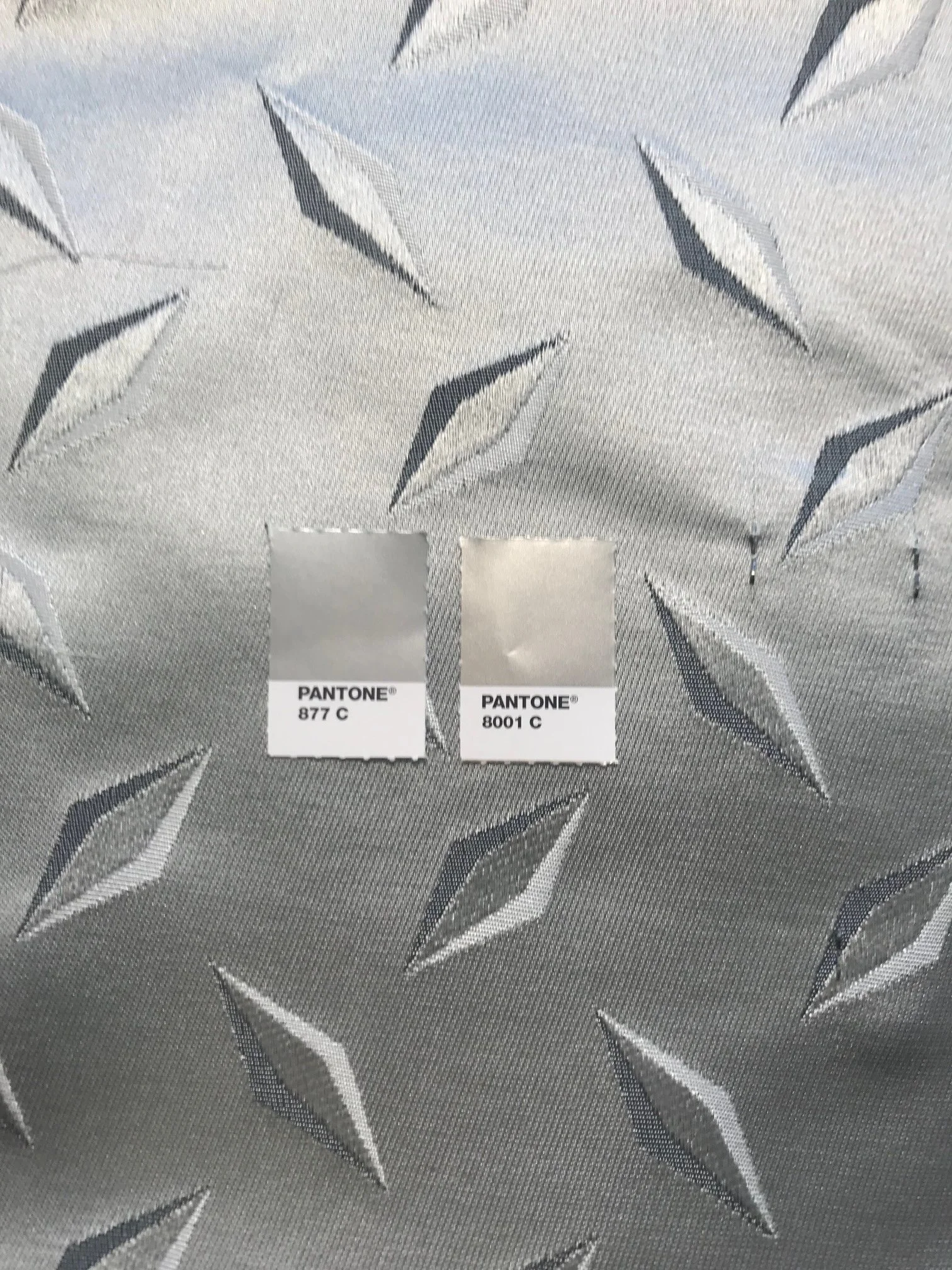 Close-up of metallic fabric with diamond-shaped patterns, and two Pantone color swatches labeled 877 C and 8001 C.