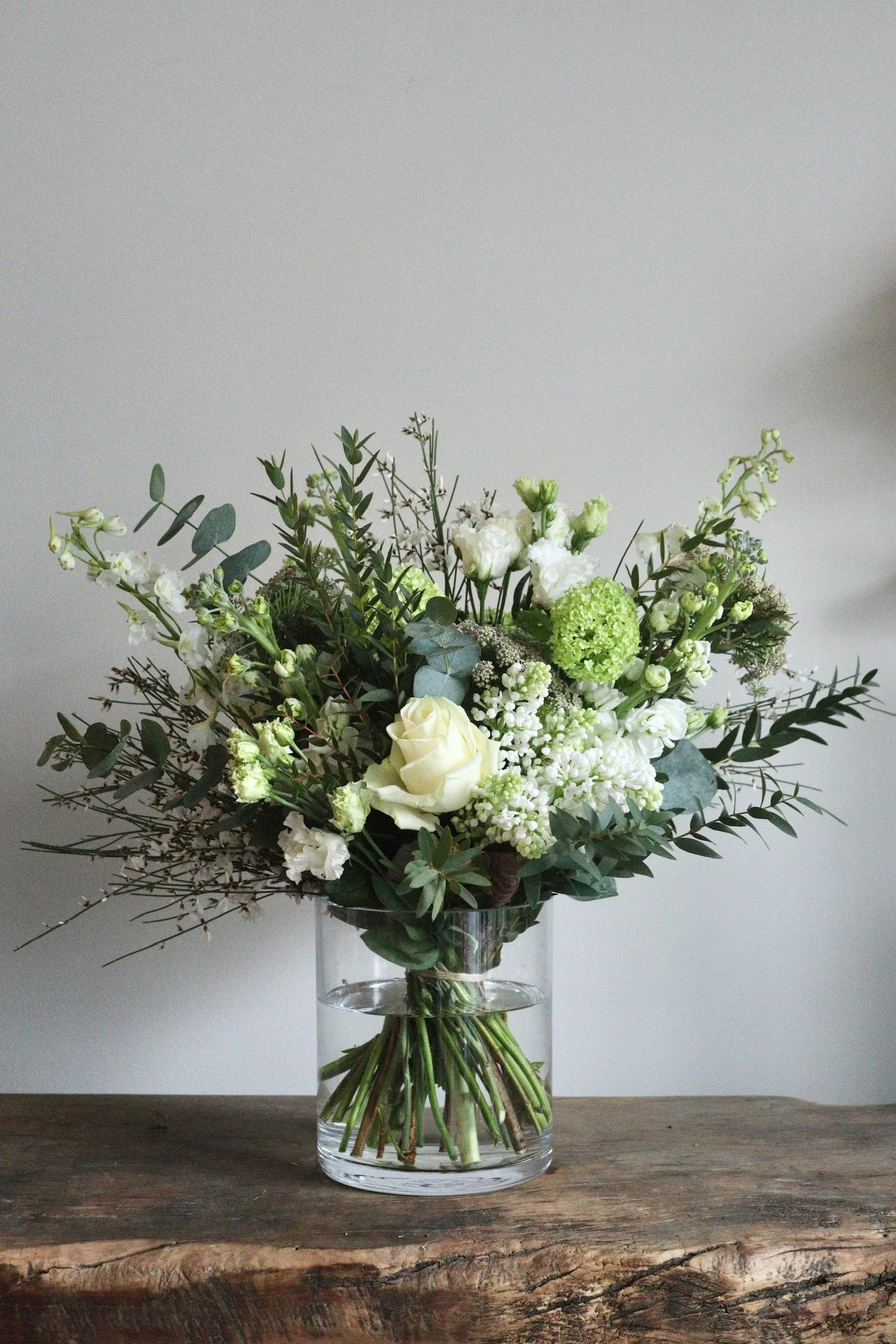 A bouquet of white and green flowers in a clear glass vase on a wooden surface.