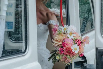 A bride holding a bouquet of pink and white flowers inside a vehicle.