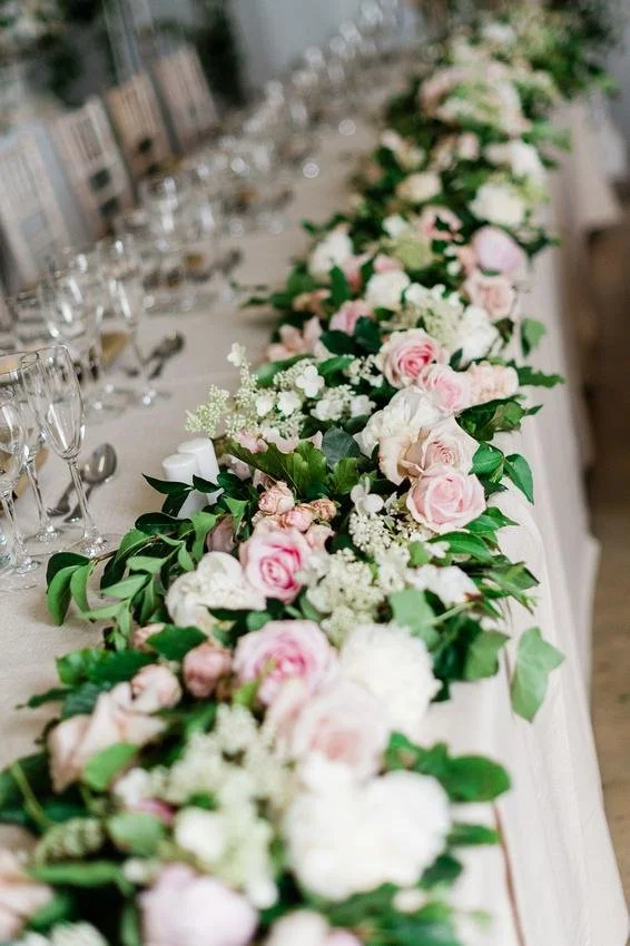 A wedding table decorated with a pink and white floral centerpiece and place settings with glasses and silverware.