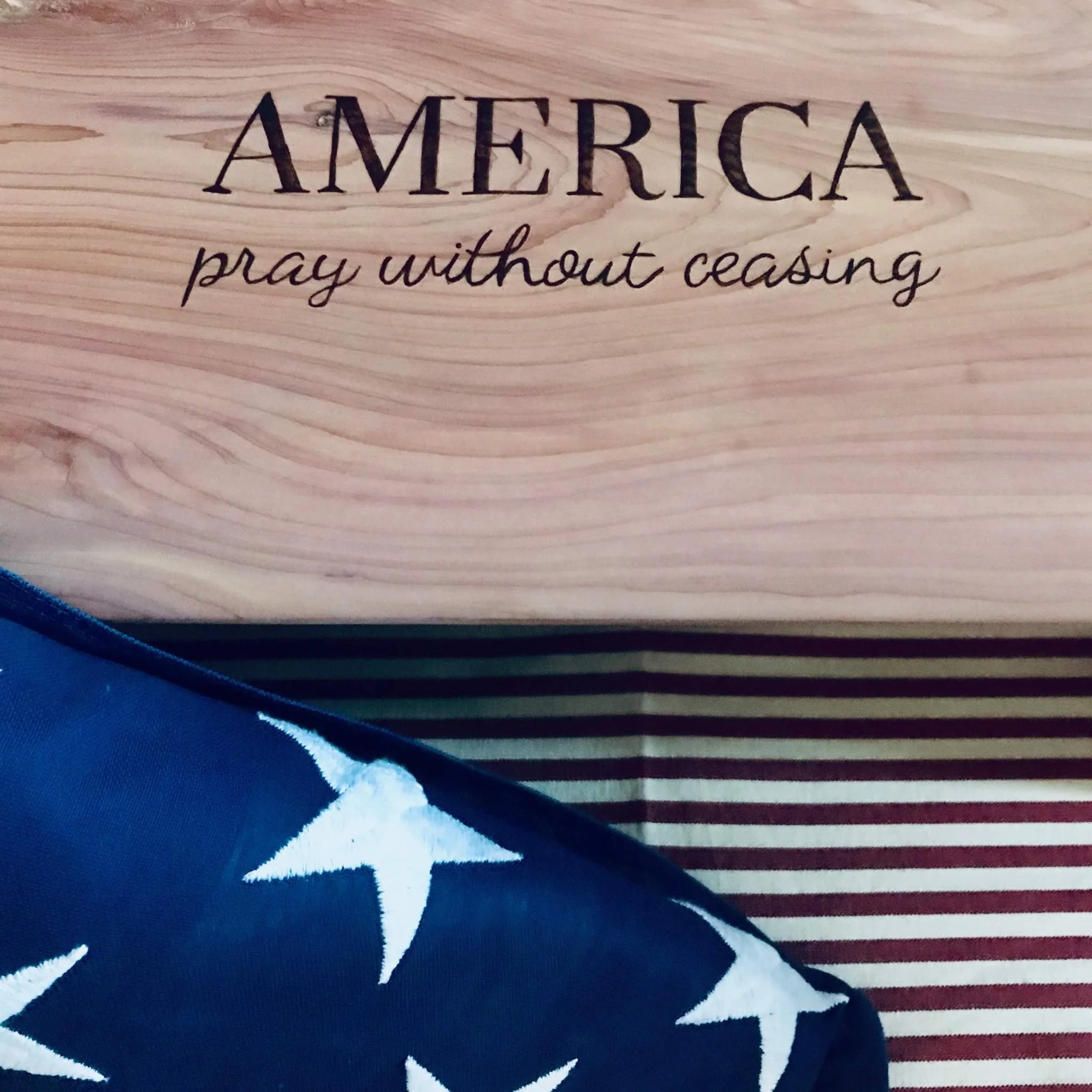 Close-up of a wooden sign with the words "AMERICA" and "pray without ceasing" engraved on it.