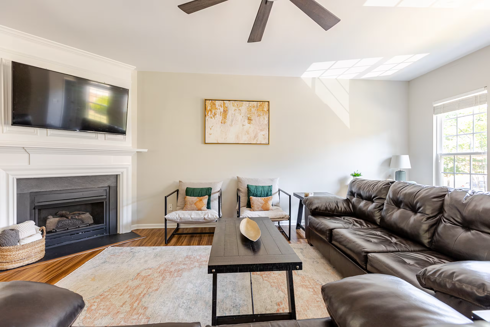 An expertly designed Northern Colorado short-term rental living room with a dark sofa, a wooden coffee table, a fireplace, a large flat-screen TV, a table lamp on a small side table, and a window with blinds letting in natural light.