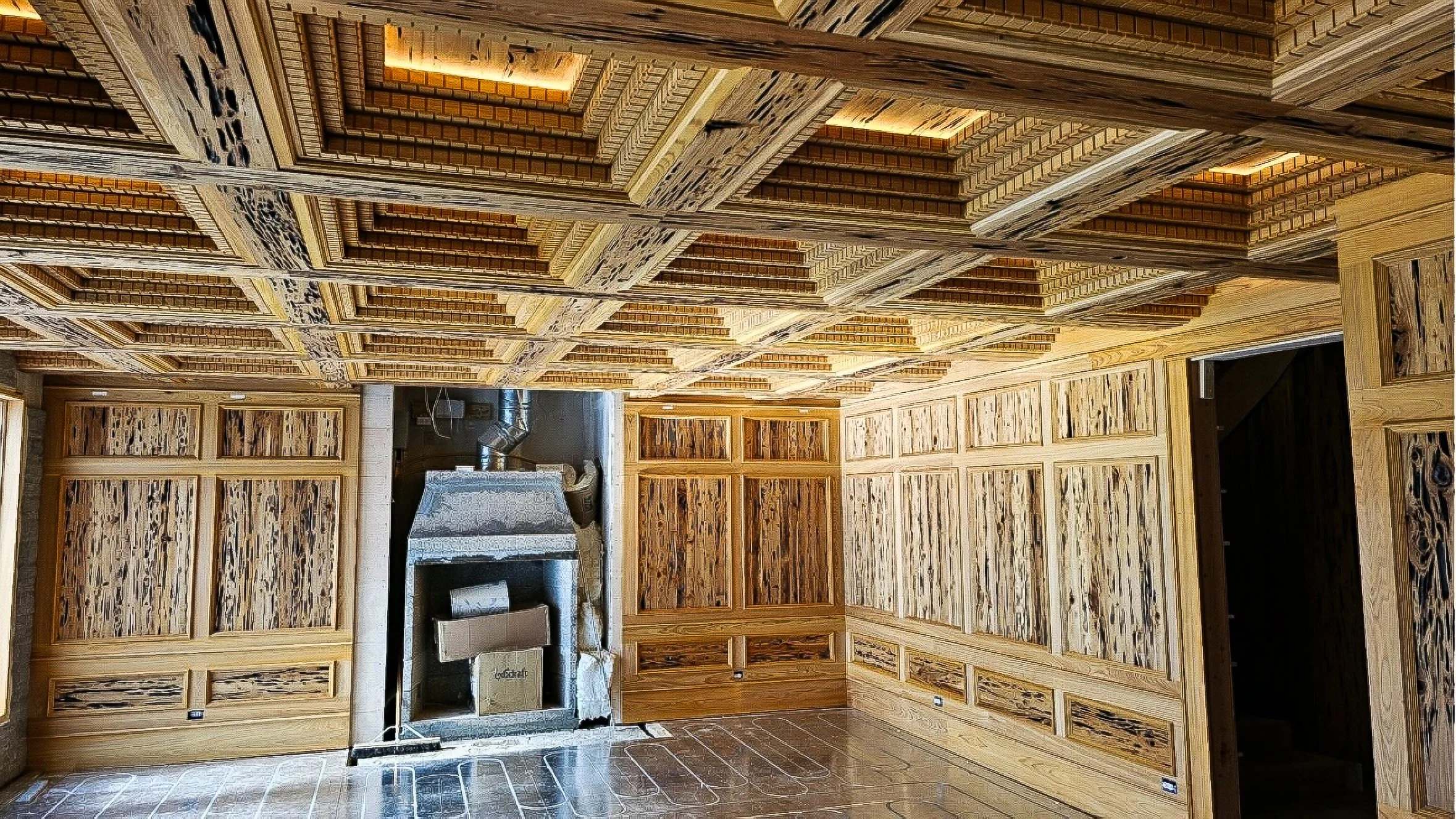 Interior of a room with wooden paneling on walls and ceiling, featuring intricate geometric patterns. There is a stone fireplace with a metal chimney in the center of one wall, and the floor is tiled with large, rectangular tiles.