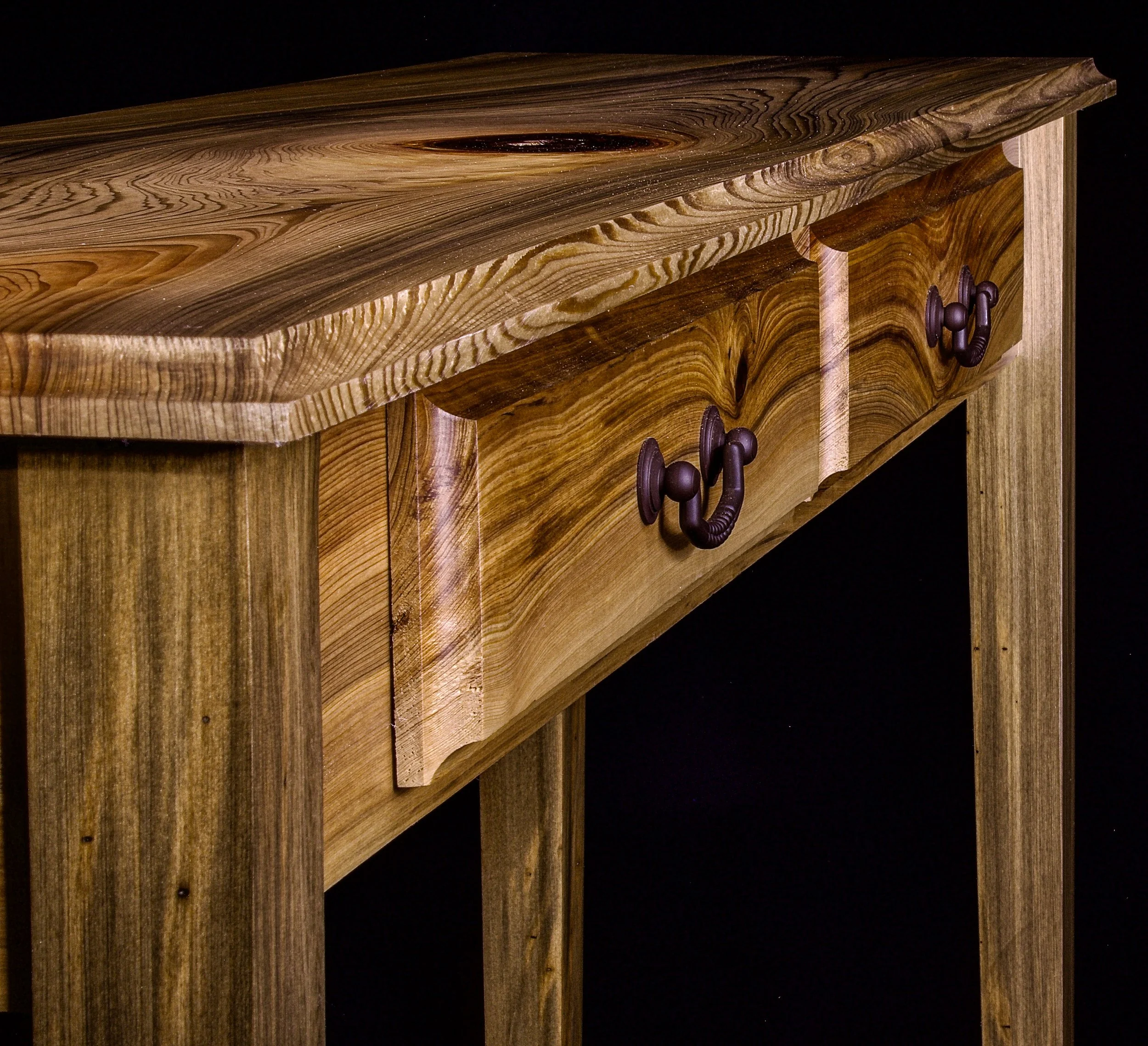 Close-up view of a wooden furniture piece with a natural grain pattern, featuring two drawers with dark purple, decorative handles.