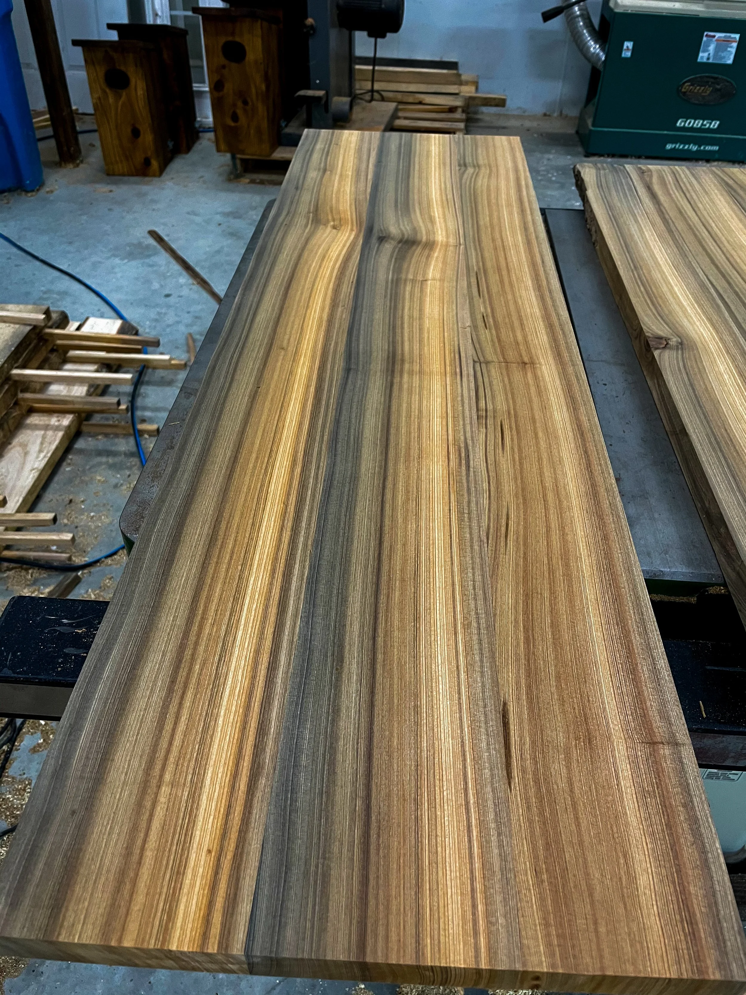 A finished, polished wooden tabletop with natural wood grain patterns in a woodworking shop.