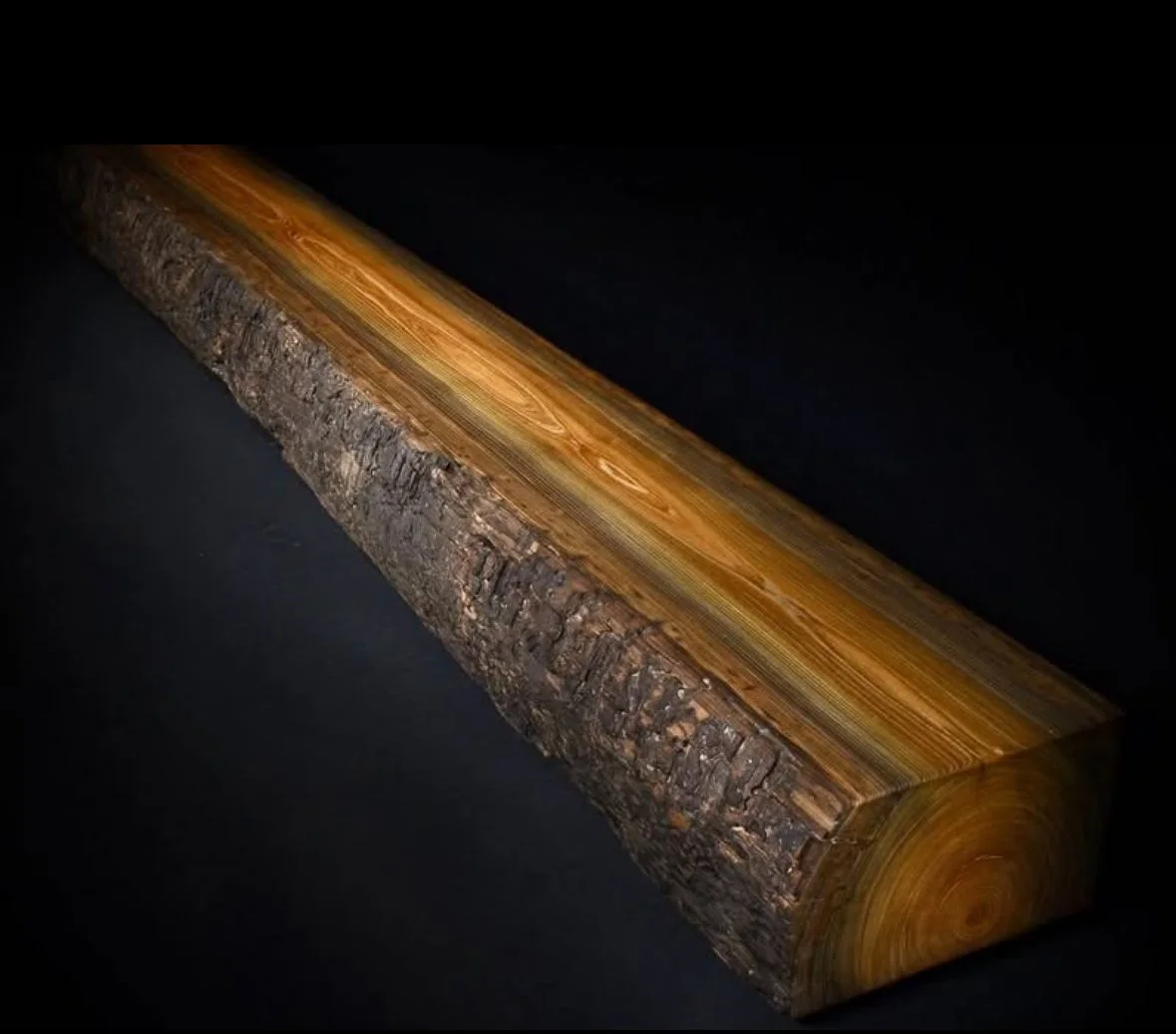 A long wooden board with a bark edge and polished surface, isolated on black background.
