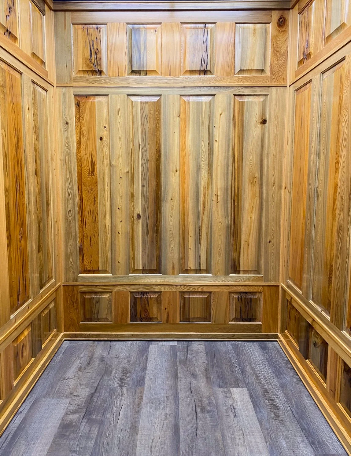 Empty wooden elevator with vertical planks on the walls and a wood grain floor.