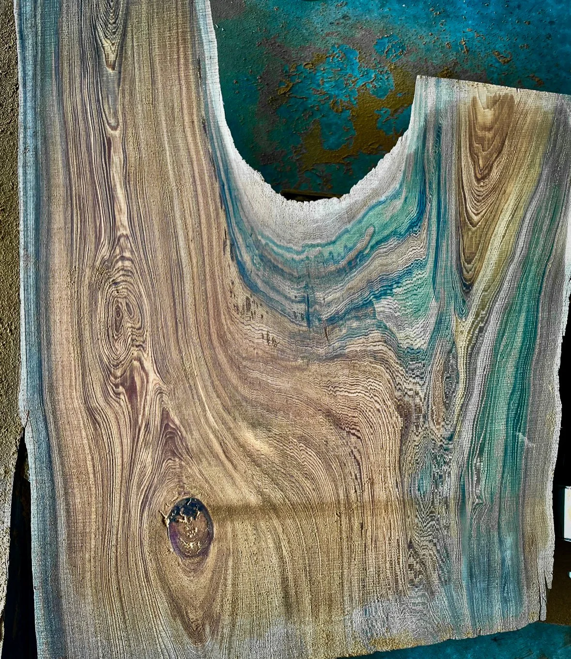 Close-up of a large slab of wood with natural grain patterns, knots, and some areas with turquoise and brown mineral deposits.