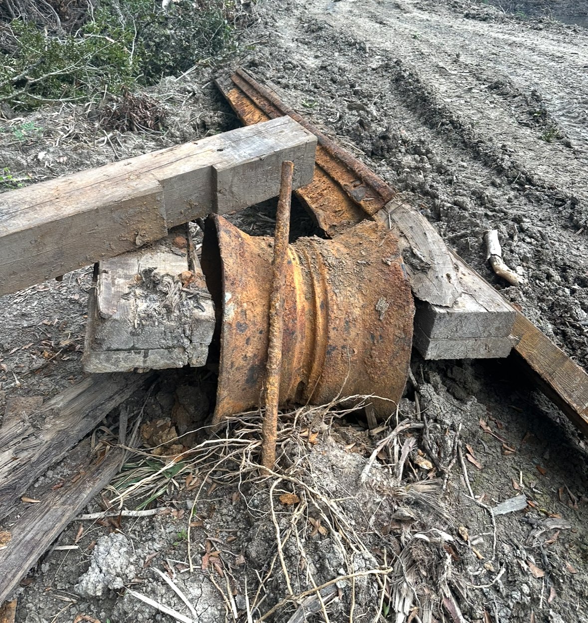 Rusty train wheel on a dirt ground, surrounded by wooden planks and debris.