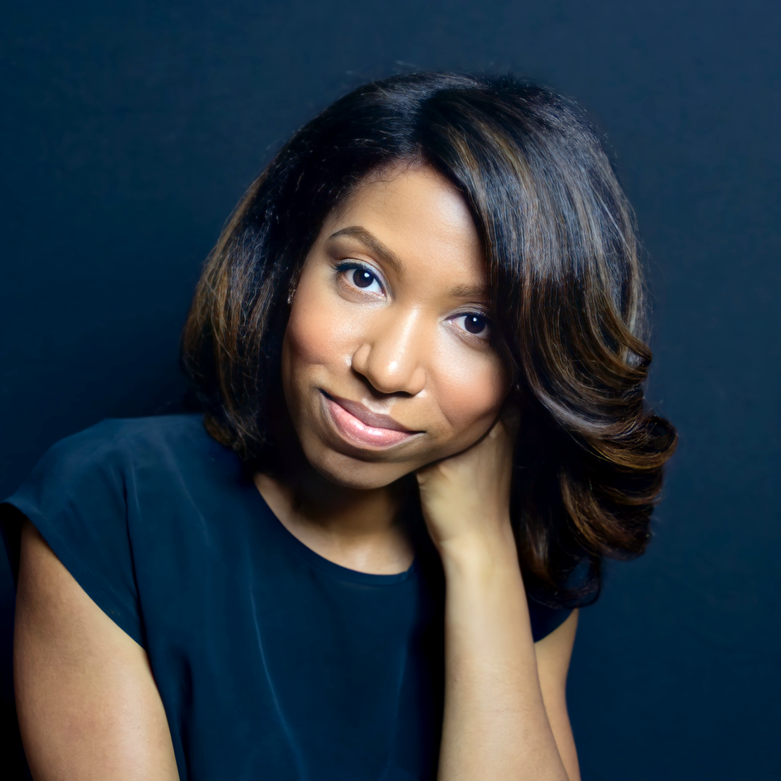 A close-up portrait of Gina S. Davis with shoulder-length wavy hair, wearing a dark top, smiling softly against a dark background.